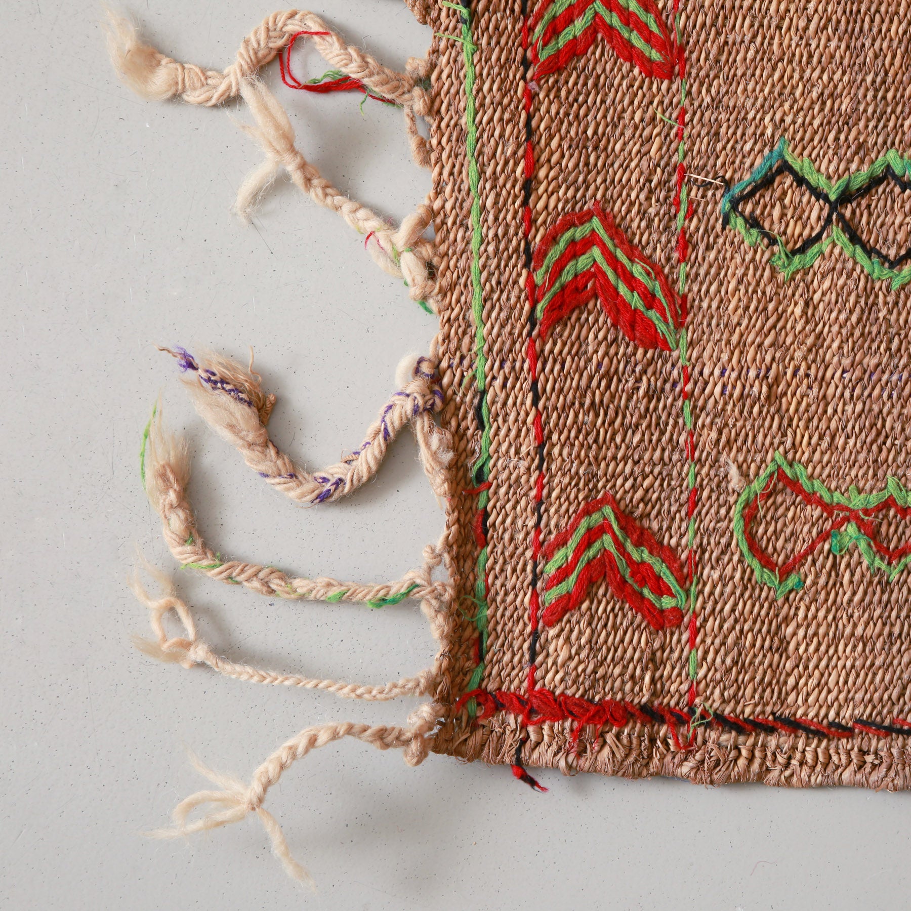 angolo di una stuoia hassira vintage con frangia lunga e ricami in lana rossa verde