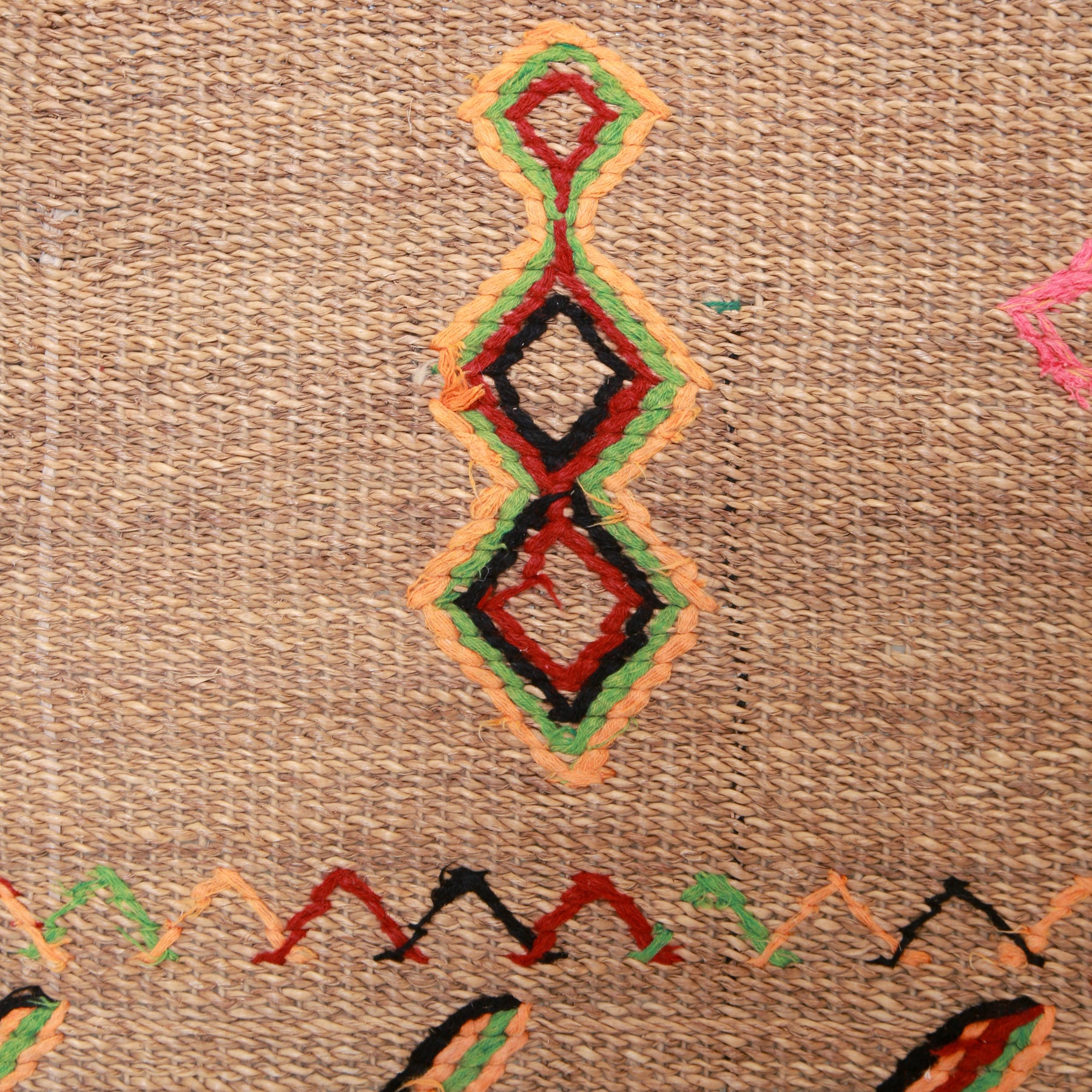 dettaglio del ricamo in lana arancione verde rosso e nere di rombi di tre rombi posizionati uno sopra l'altro suo una stuoia in paglia di palma vintage