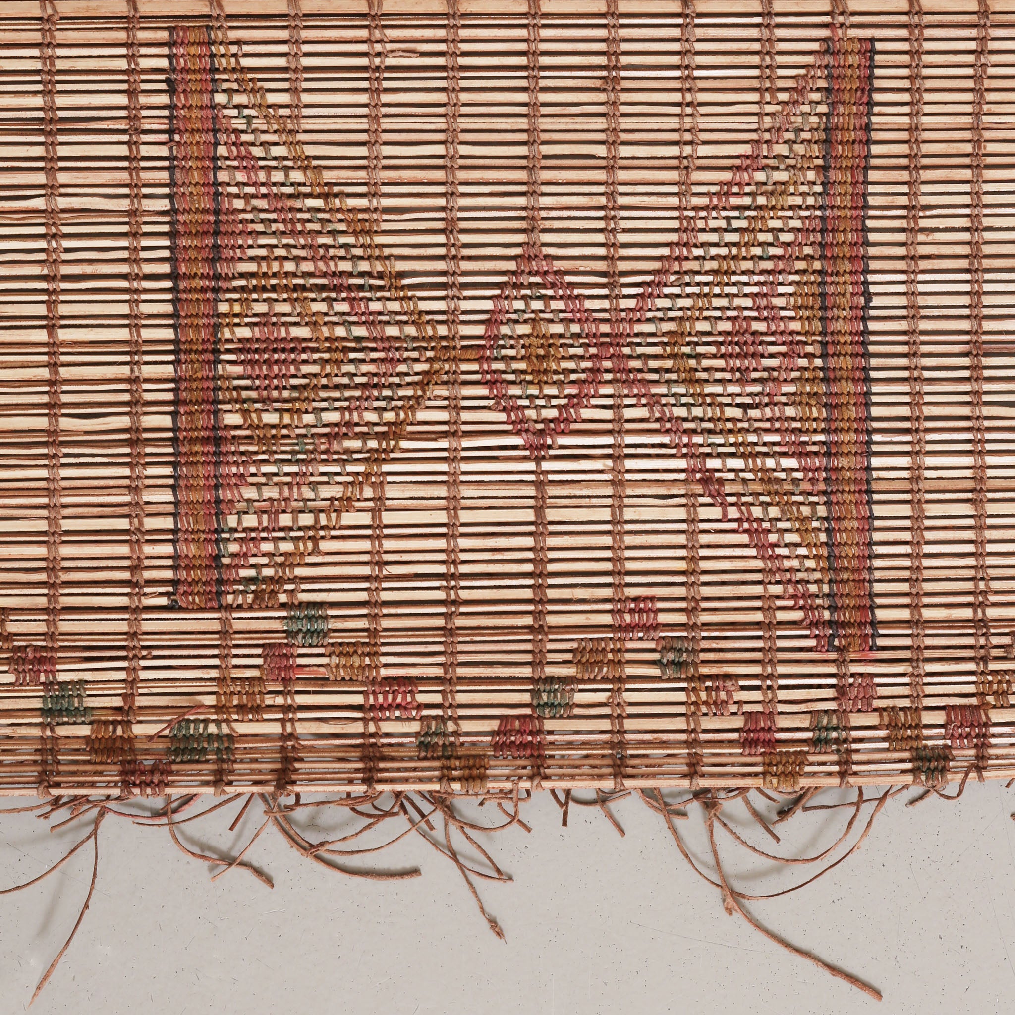 dettaglio di un simbolo che sembra una clessidra lavorato intrecciando fili di cuoio colorato su una stuioa