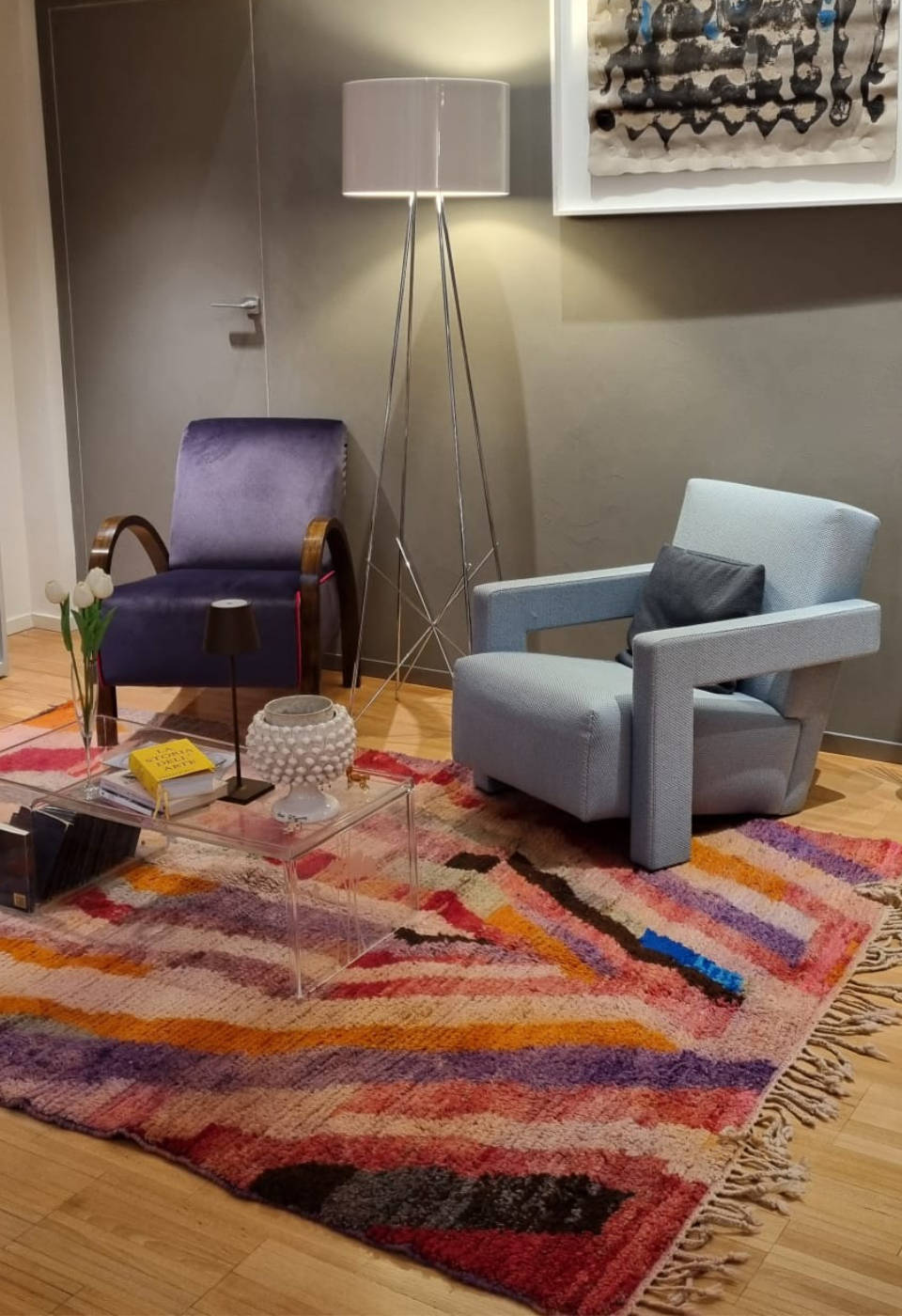 Tapis berbère marocain vibrant avec motif abstrait coloré dans un salon moderne, complétant des fauteuils violet et bleu, une lampe tripode et une table basse transparente