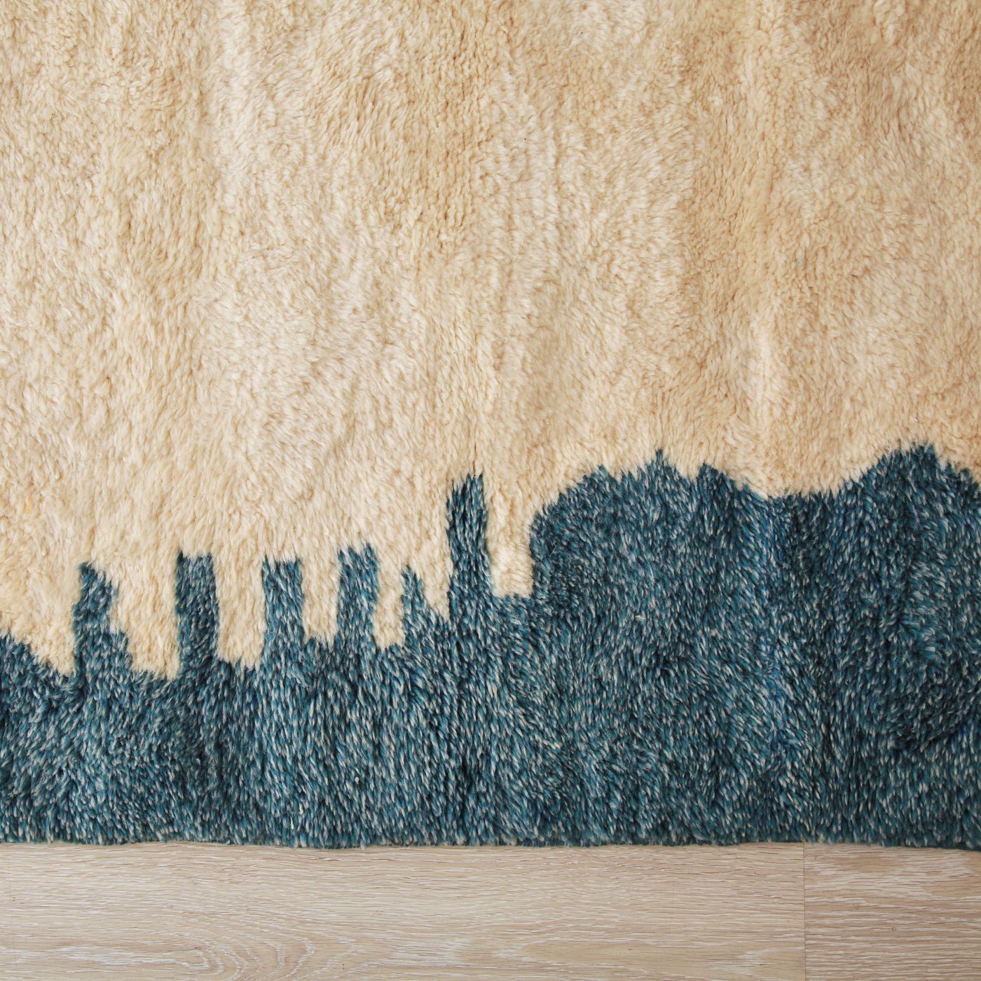 Tapis marocain berbere Beni Mrirt avec motif skyline de ville. Design en laine beige et bleu foncé, texture douce et duveteuse. Partie supérieure beige avec silhouette urbaine bleue dans la partie inférieure. Élégant tapis artisanal sur plancher en bois clair.