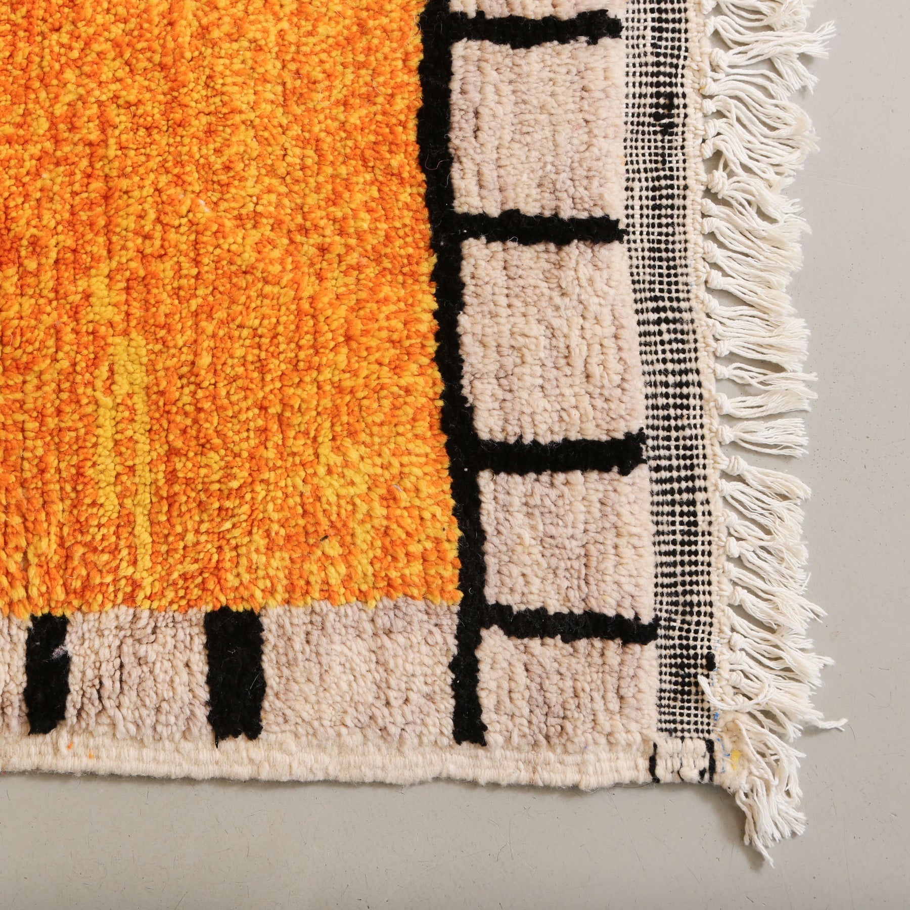 angolo di tappeto azilal con lana tinta di giallo e arancione e cornice con quadrati bianchi con bordi neri