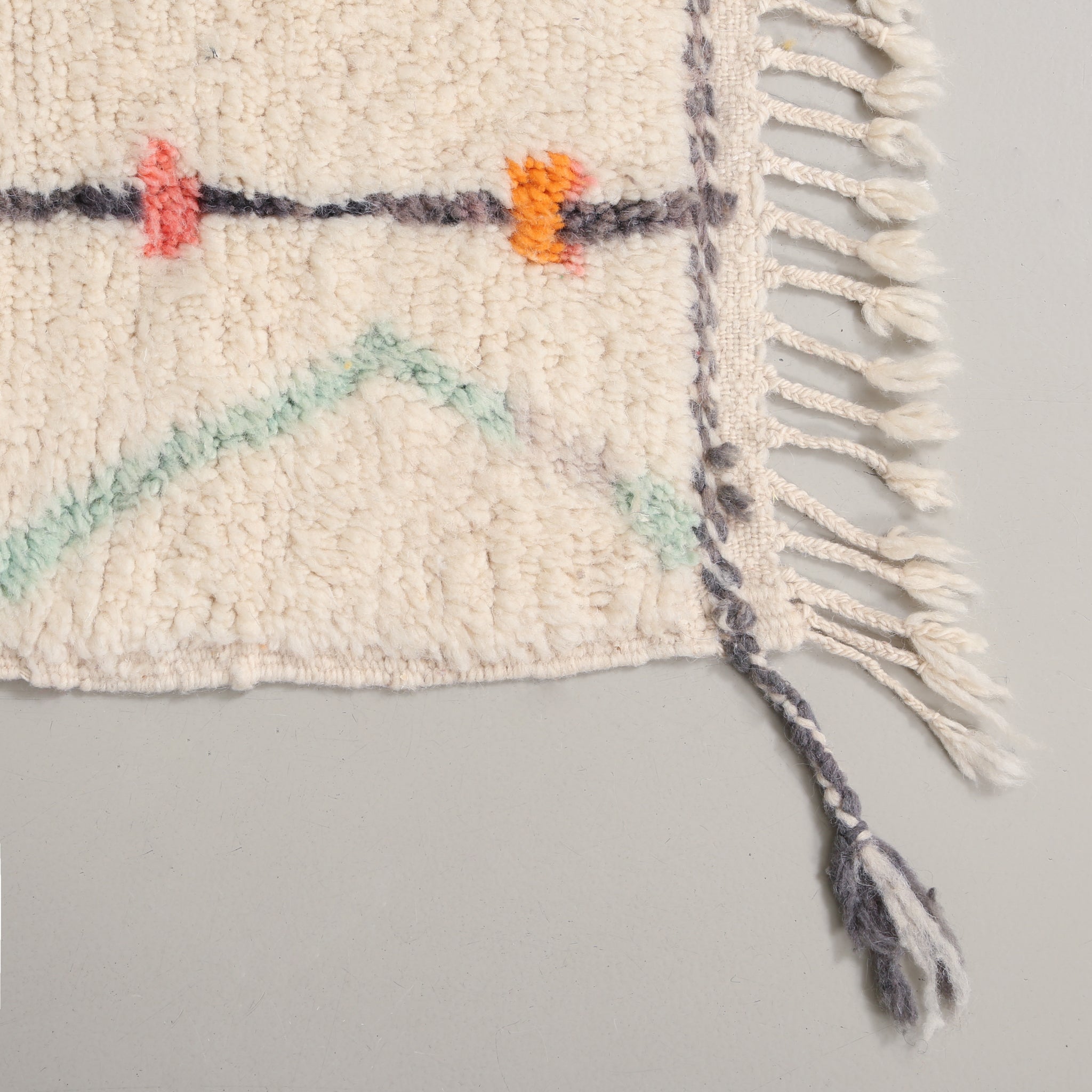 Angolo di un tappeto azilal. si notano la lana morbida del pelo, i colori pastello e la frangia