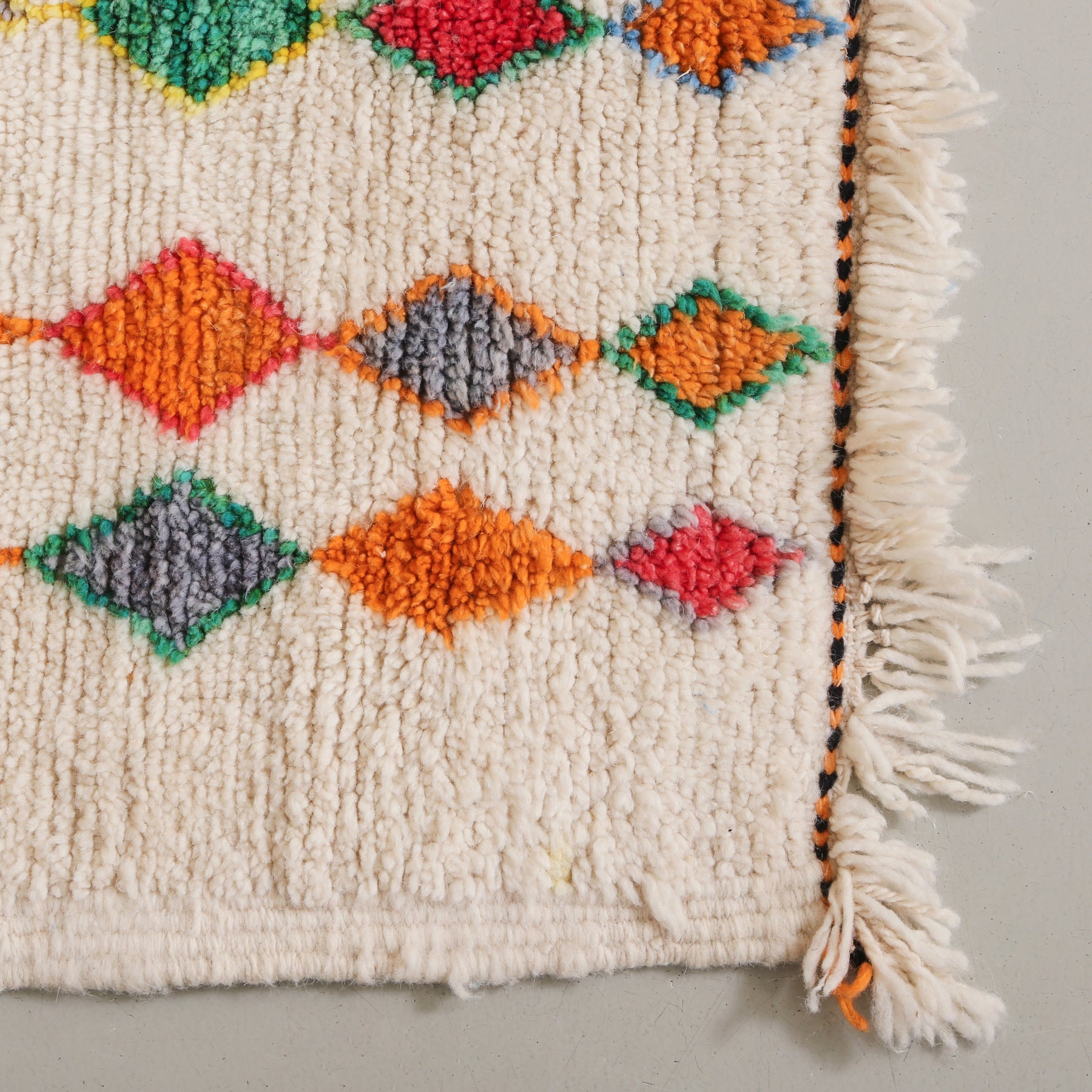 angolo di un tappeto con forme geometriche colorate e frangia corta
