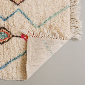 dettaglio del retro di un tappeto in lana su base chiara con rombi e linee colorate