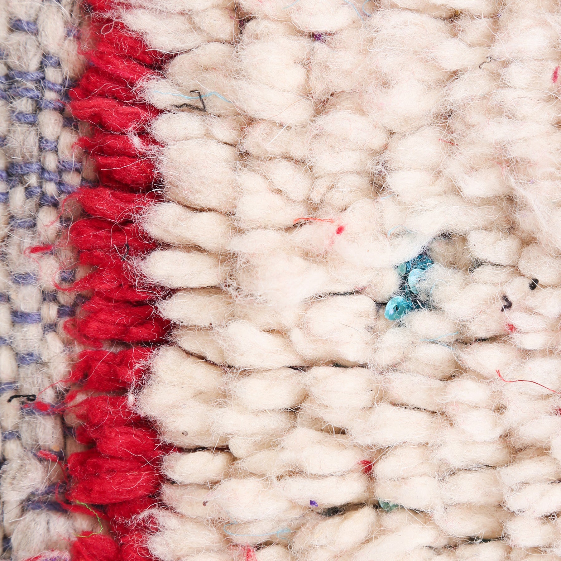 dettaglio dei nodi di lana avorio e rossa con delle paiette azzurre che spuntano
