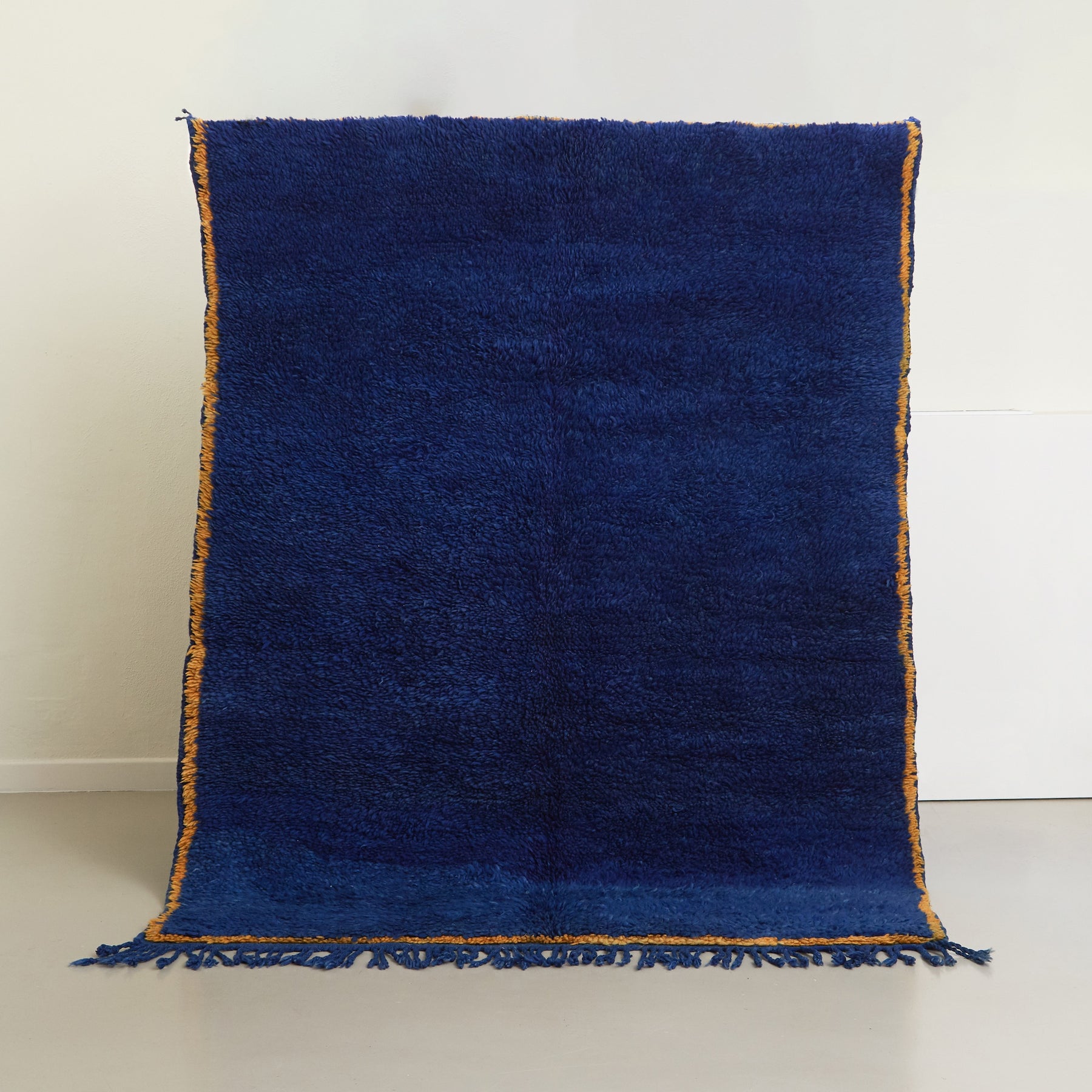 tappeto beni mguild blu con bordo zafferano e frangia blu appeso