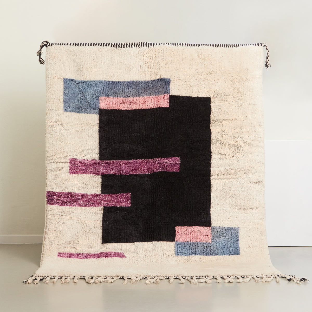 tappeto beni mrirt con design contemporaneo a rettangoli colorati neri viola rosa e azzurro su base in lana bianca appeso
