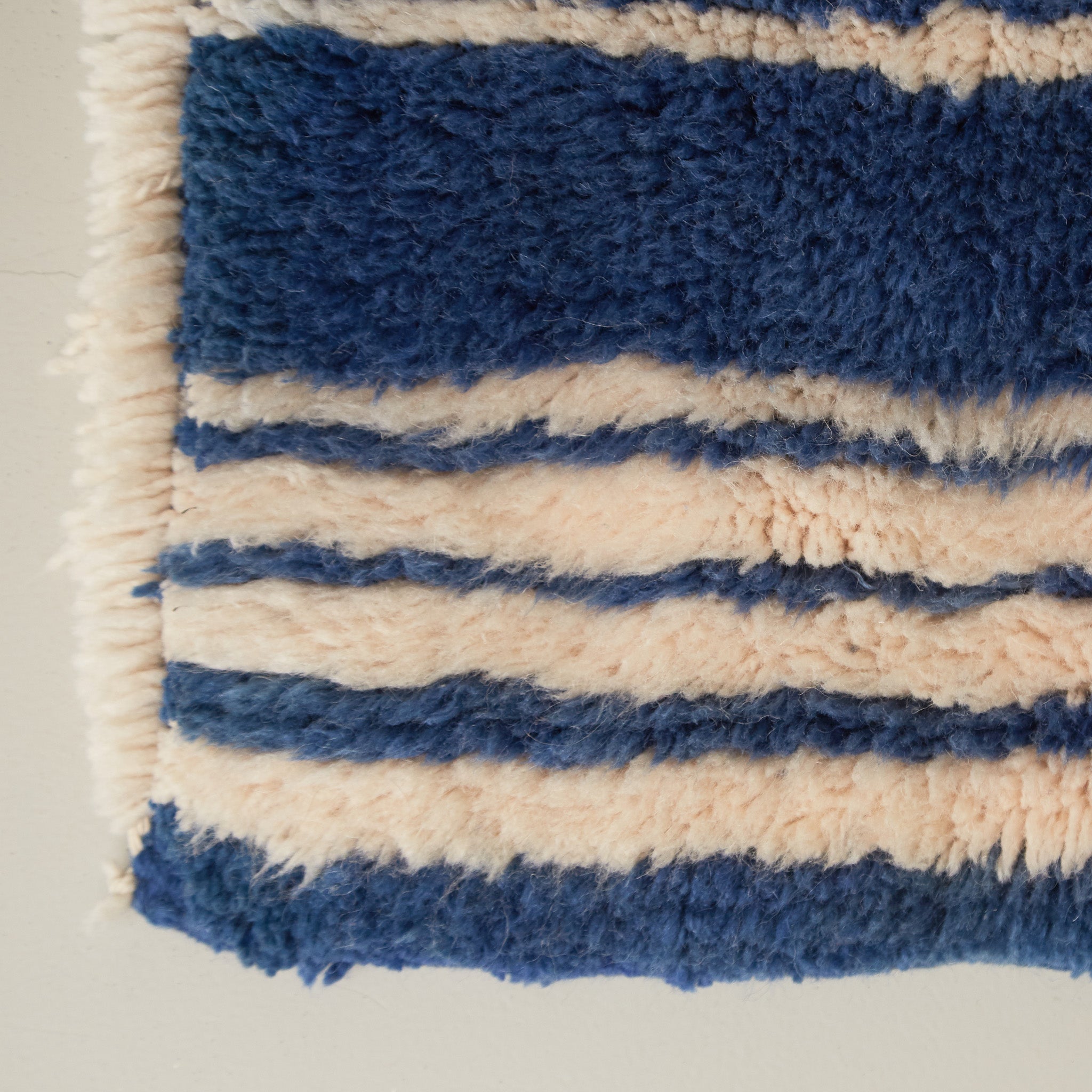 angolo di un tappeto beni mrirt realizzato con morbida lana di colore blu con righe bianche