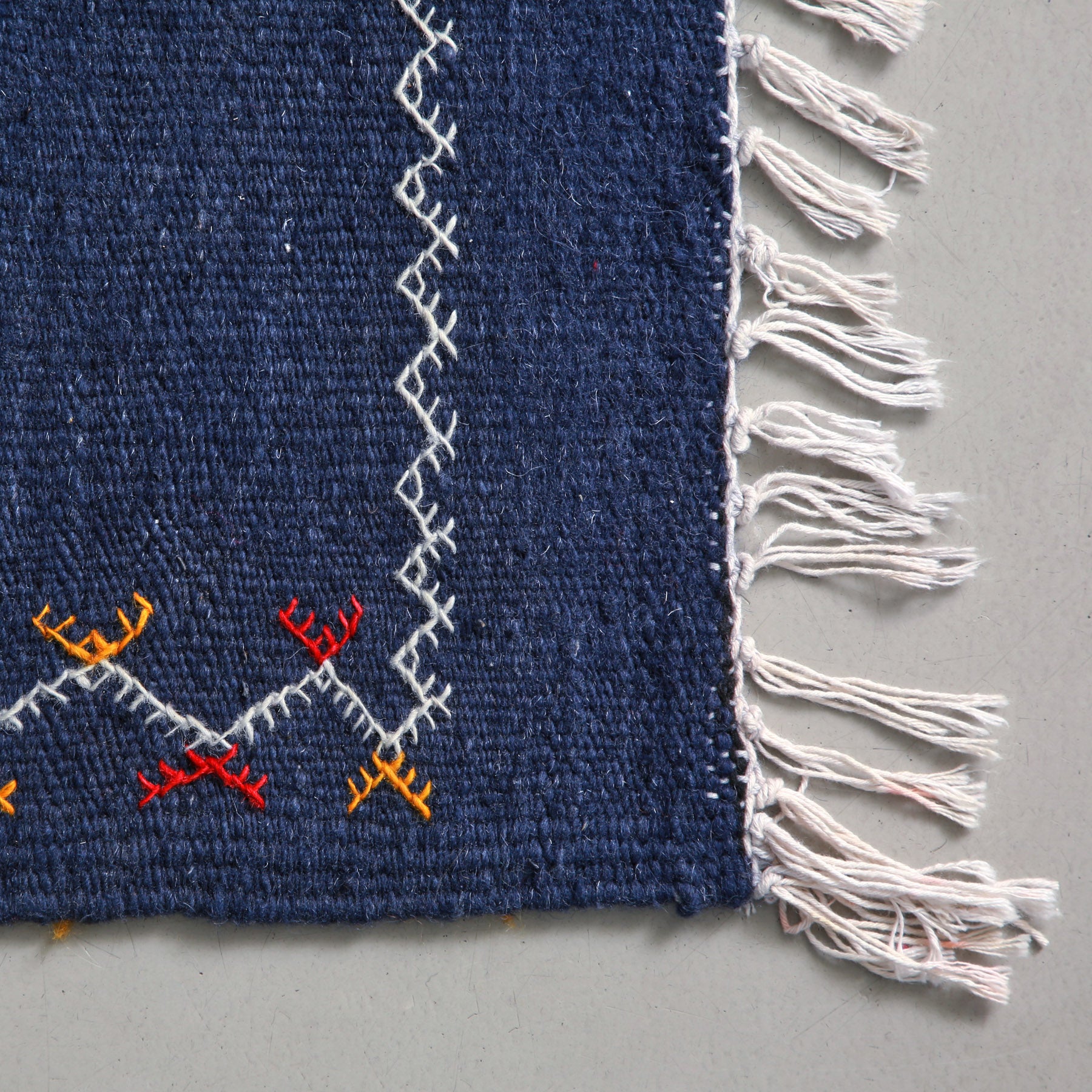 dettaglio dell'angolo con una cornice ricamata e delle frangia sottile di un tappeto artigianale marocchino a tessitura piatta colore blu
