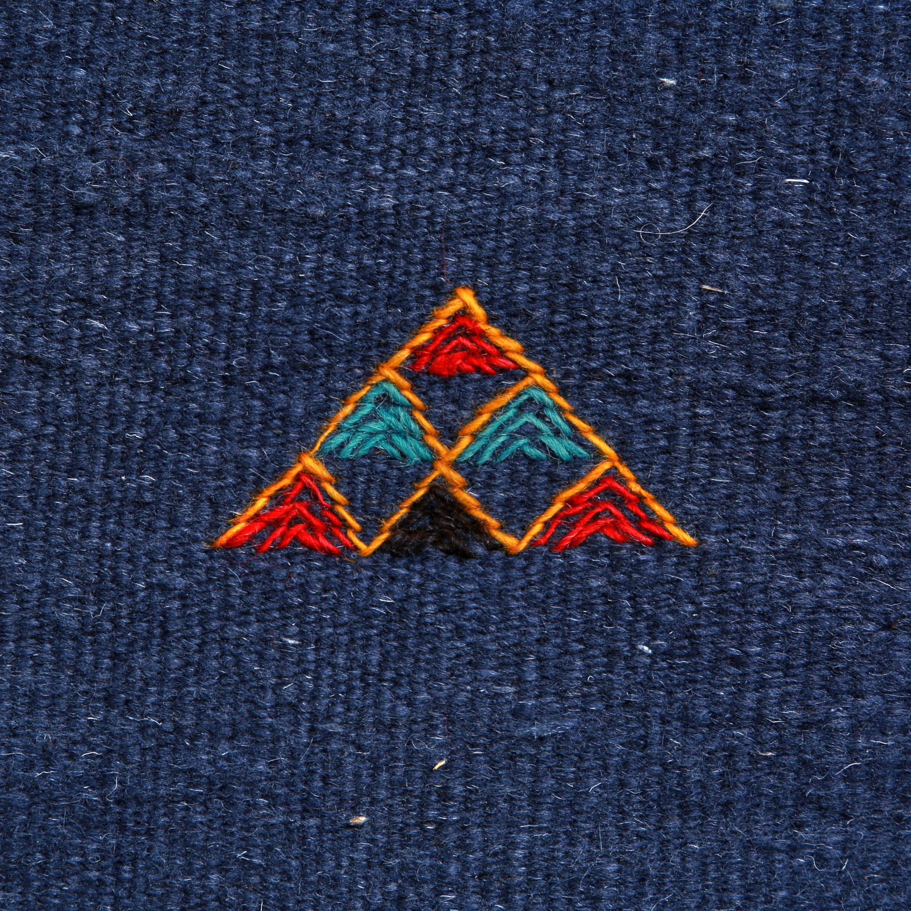 dettaglio di un simbolo amazigh a forma di piramide ricamato su un tappeto artigianale marocchino a tessitura piatta blu