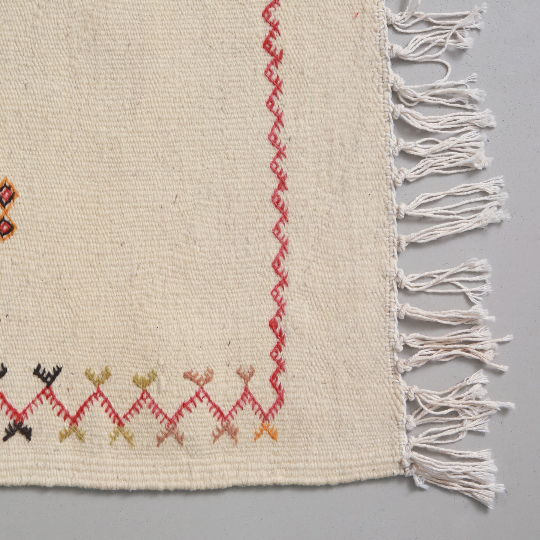angolo con cornice a zig zag rossa e frangia corta e sottile di un  tappeto marocchino akhnif a tessitura bianca in lana bianca