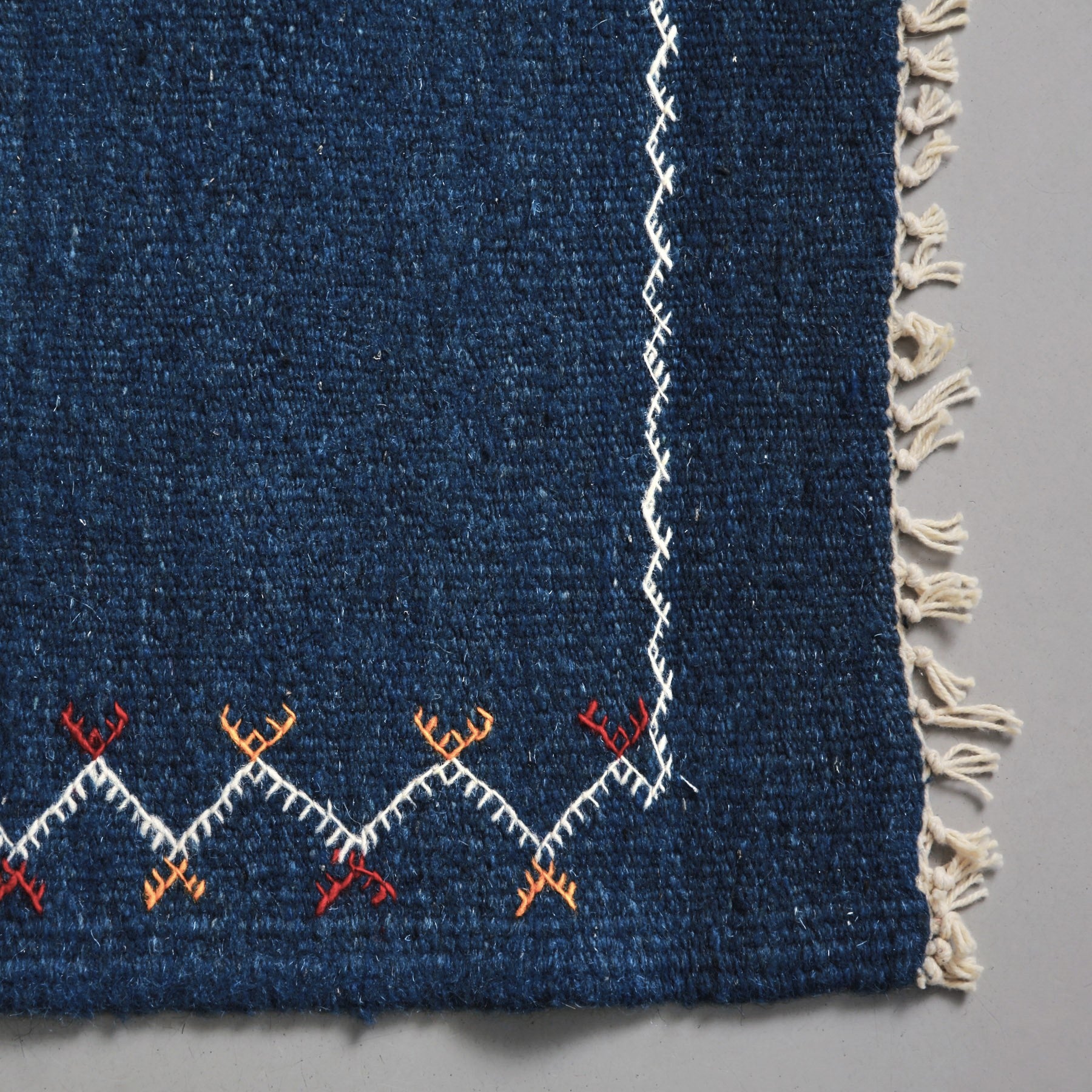 dettaglio della corta frangia sottile e della cornice ricamata in bianca di un Tappeto marocchino akhnif a tessitura piatta  blu