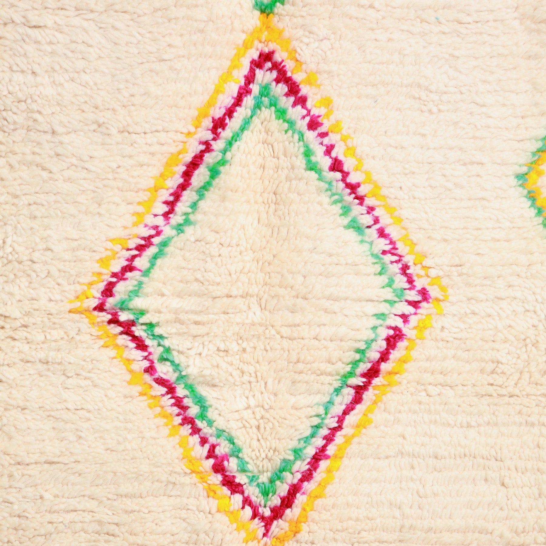 dettaglio di unn serie di rombi messi uno dentro l'altro di colore giallo, fucsia e verde su base chiara di un tappeto marocchino azilal 