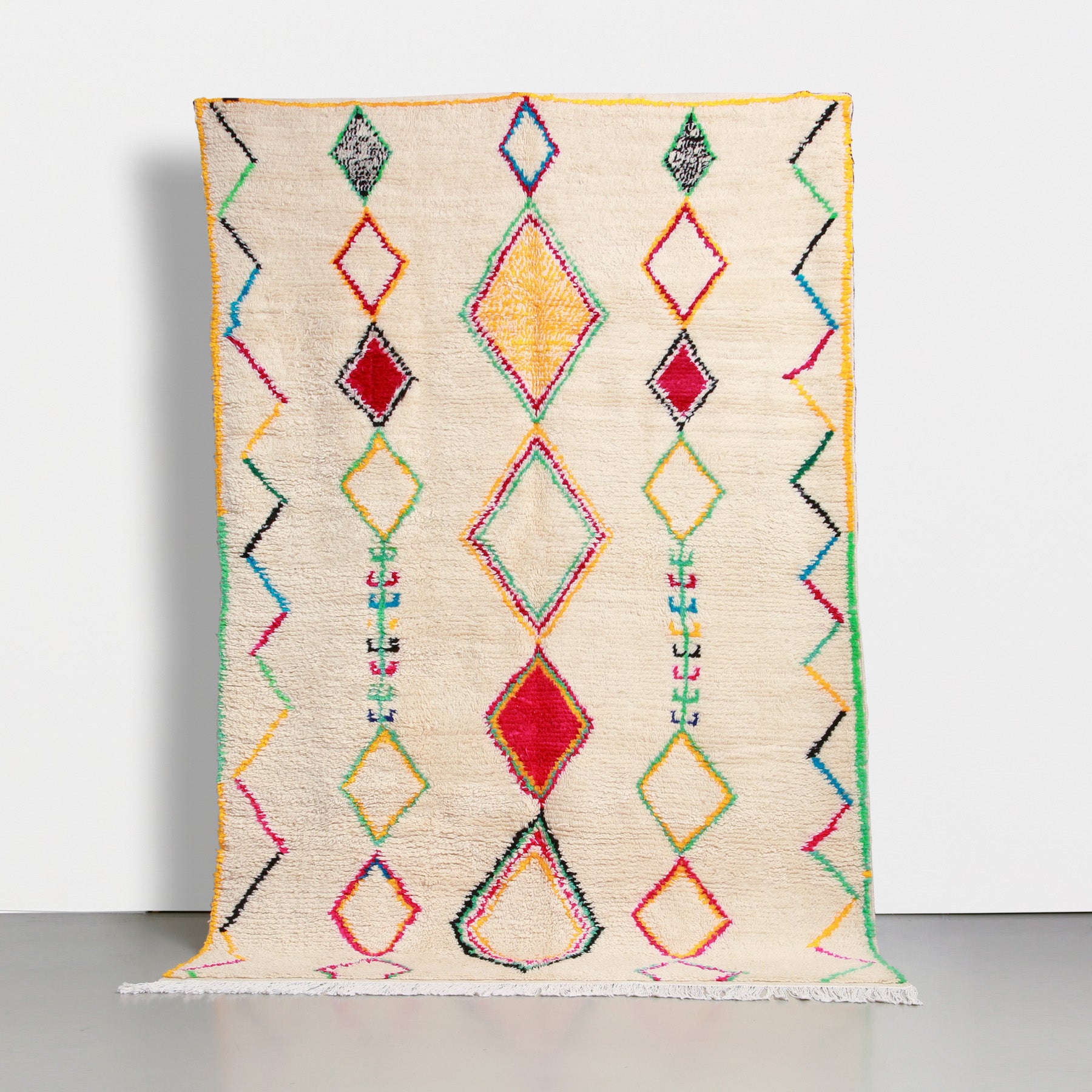 tappeto marocchino azilal realizzato a mano con lana color panna e simboli amazigh dai colori sgarguianti. ci sono 3 righe verticali di rombi e una cornice a zig zag