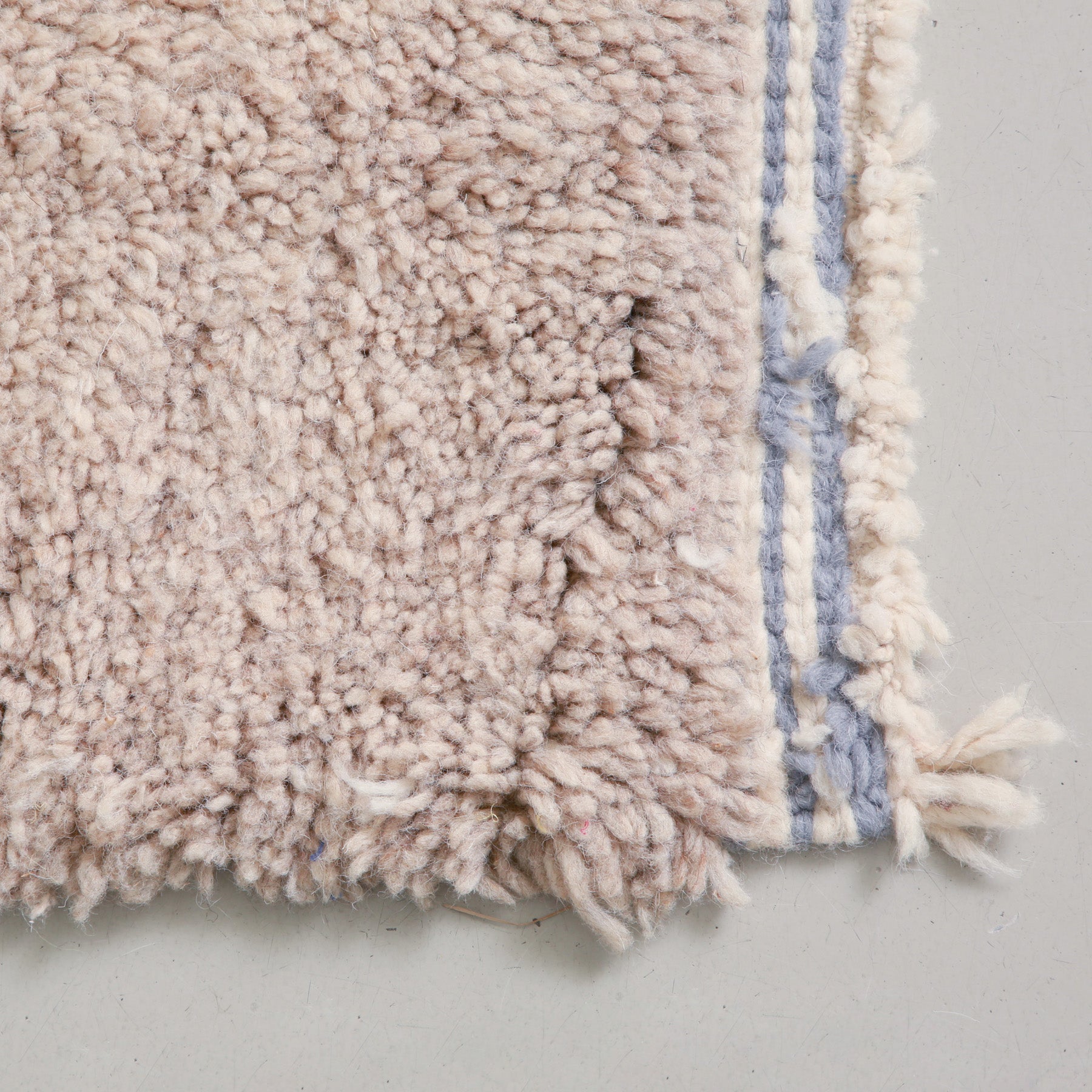 angolo di colore grigio di un tappeto marocchino con bordo a righe bianche e blu e frangia corta