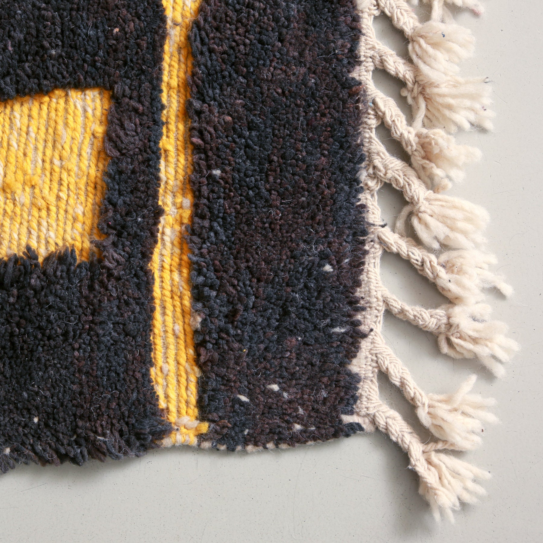 dettaglio dei un angolo con lana annodata dalle sfumature gruigio scure e marrone con delle parti in lana intrecciata guialla di un tappeto marocchino beni ourain realizzato a mano