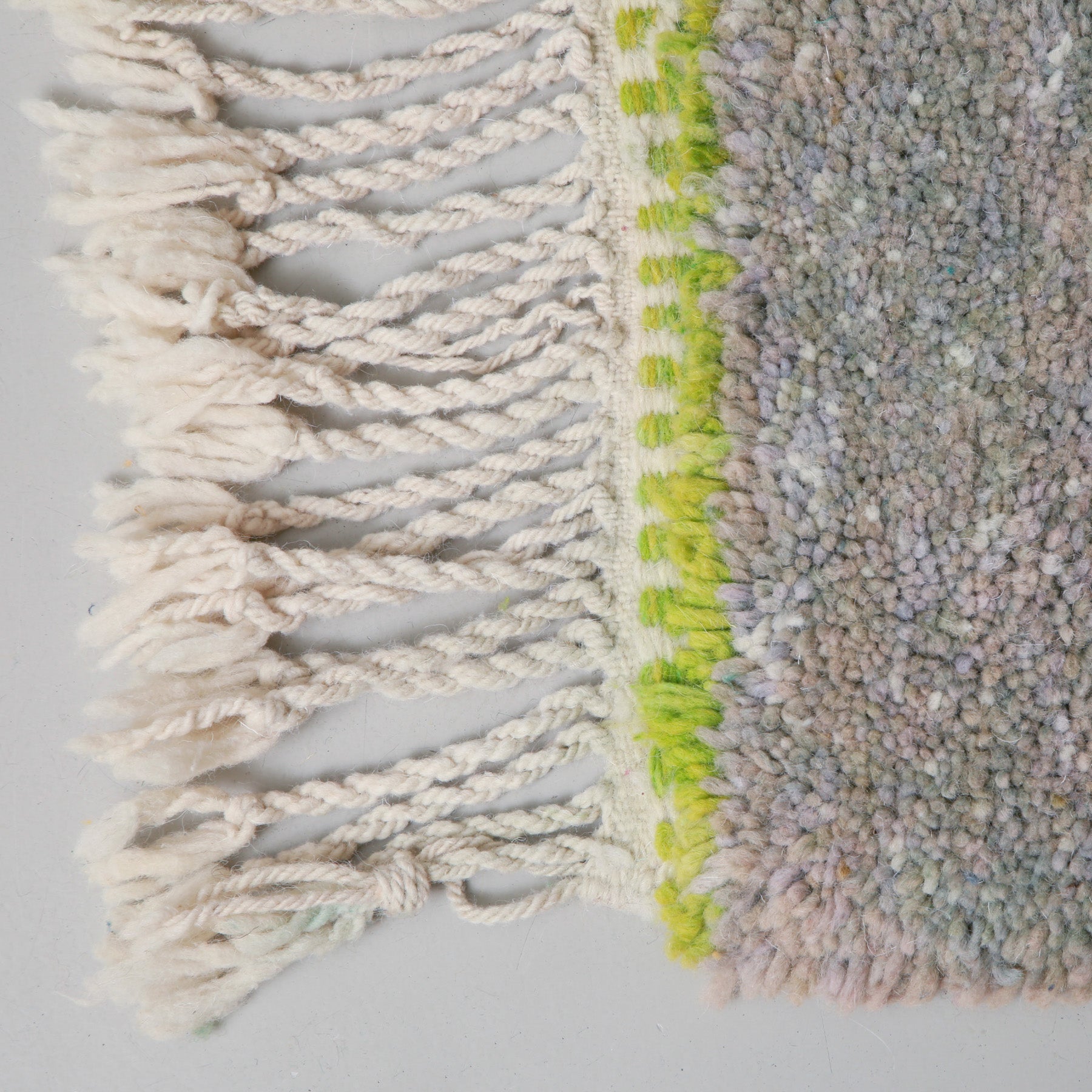 angolo di un tappeto marocchino beni ourain realizzato a mano. in questo dettaglio si vede la lana di colore grigio e l'attaccatura della frangia di colore verde