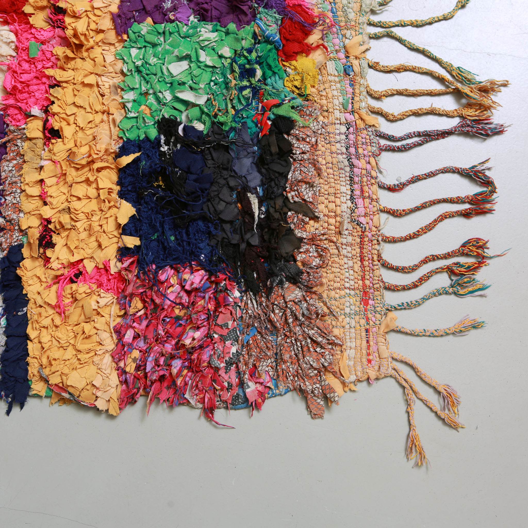 Angolo e frange intrecciate multicolori del tappeto berbero Boucherouite vintage, mostrando la transizione tra trama tridimensionale di tessuti riciclati e base tessile
