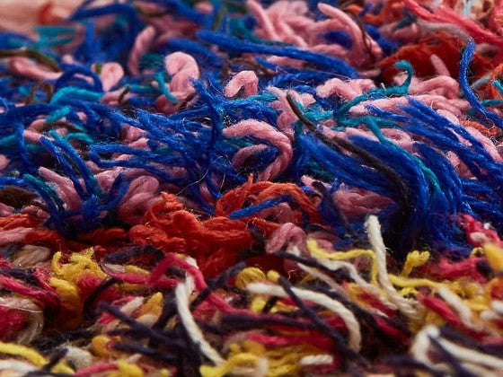 Dettaglio di un tappeto in cui convivono filamenti di diverse tinte e tessuti, prodotto con la tecnica del riciclo