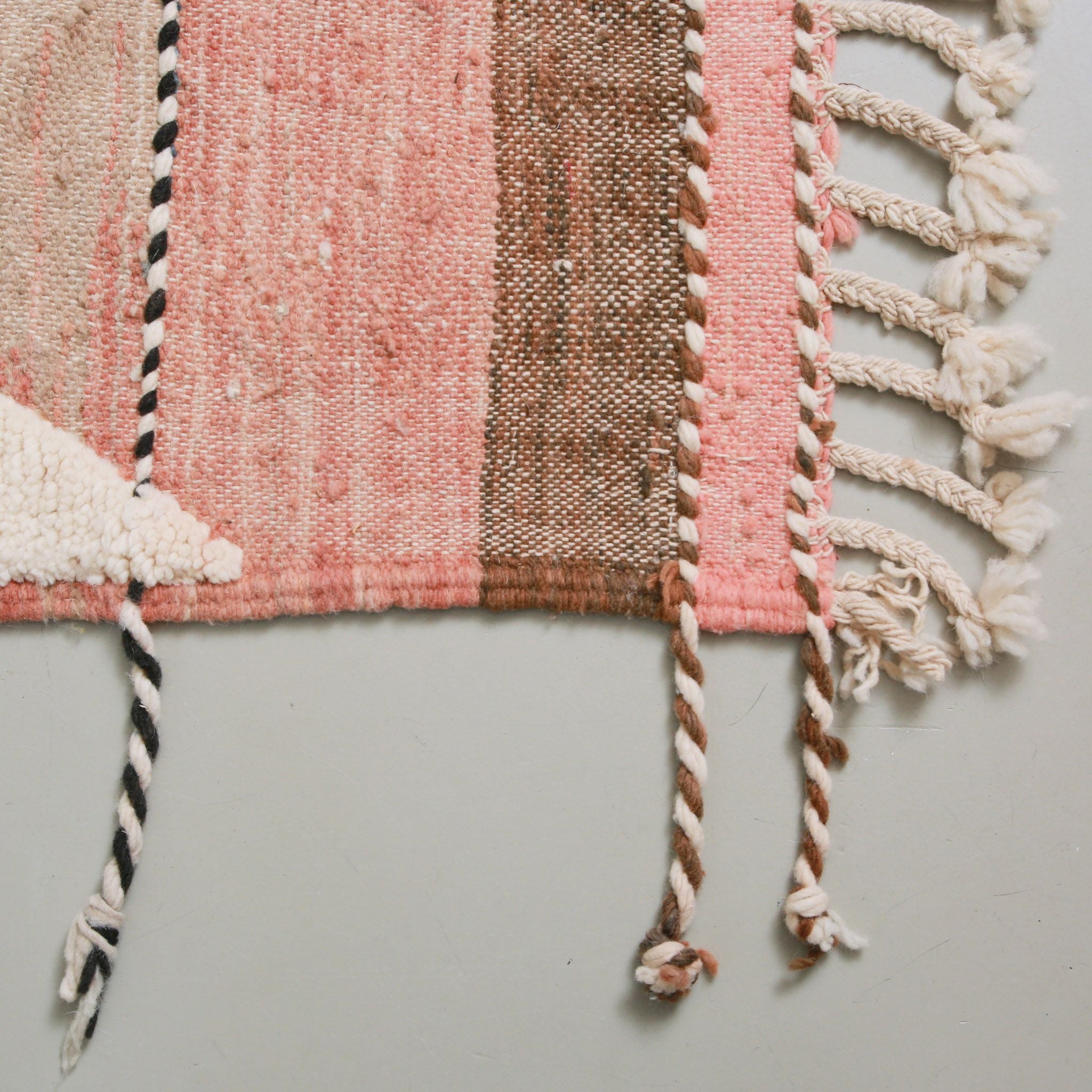 Dettaglio del bordo di tappeto Boujaad con tessitura piatta rosa e terracotta e frange intrecciate bianche e marroni tipiche della tradizione Amazigh