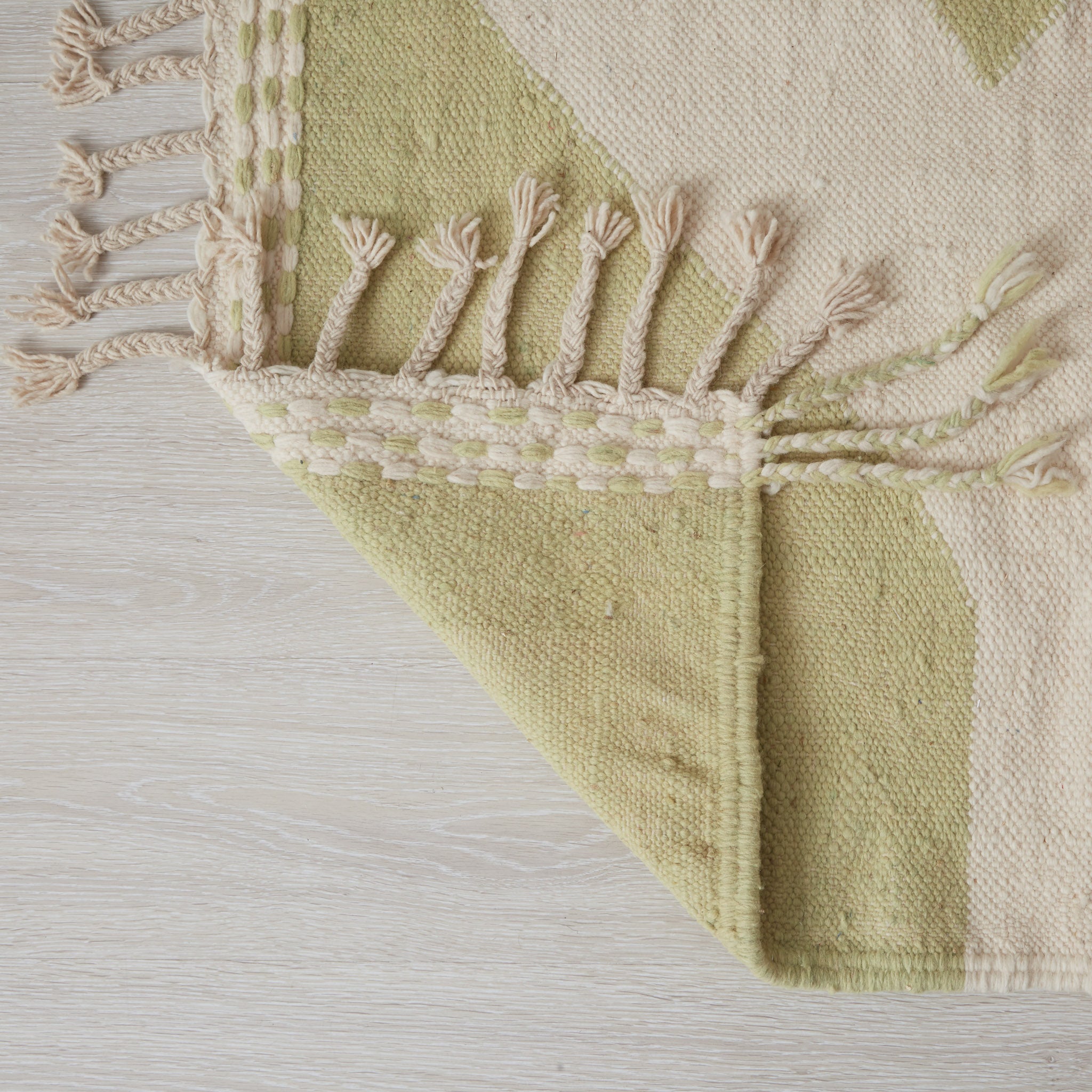 Particolare dell'angolo del tappeto Hanbel con nappe decorative e motivo geometrico, tessitura piatta tradizionale in verde salvia e avorio naturale