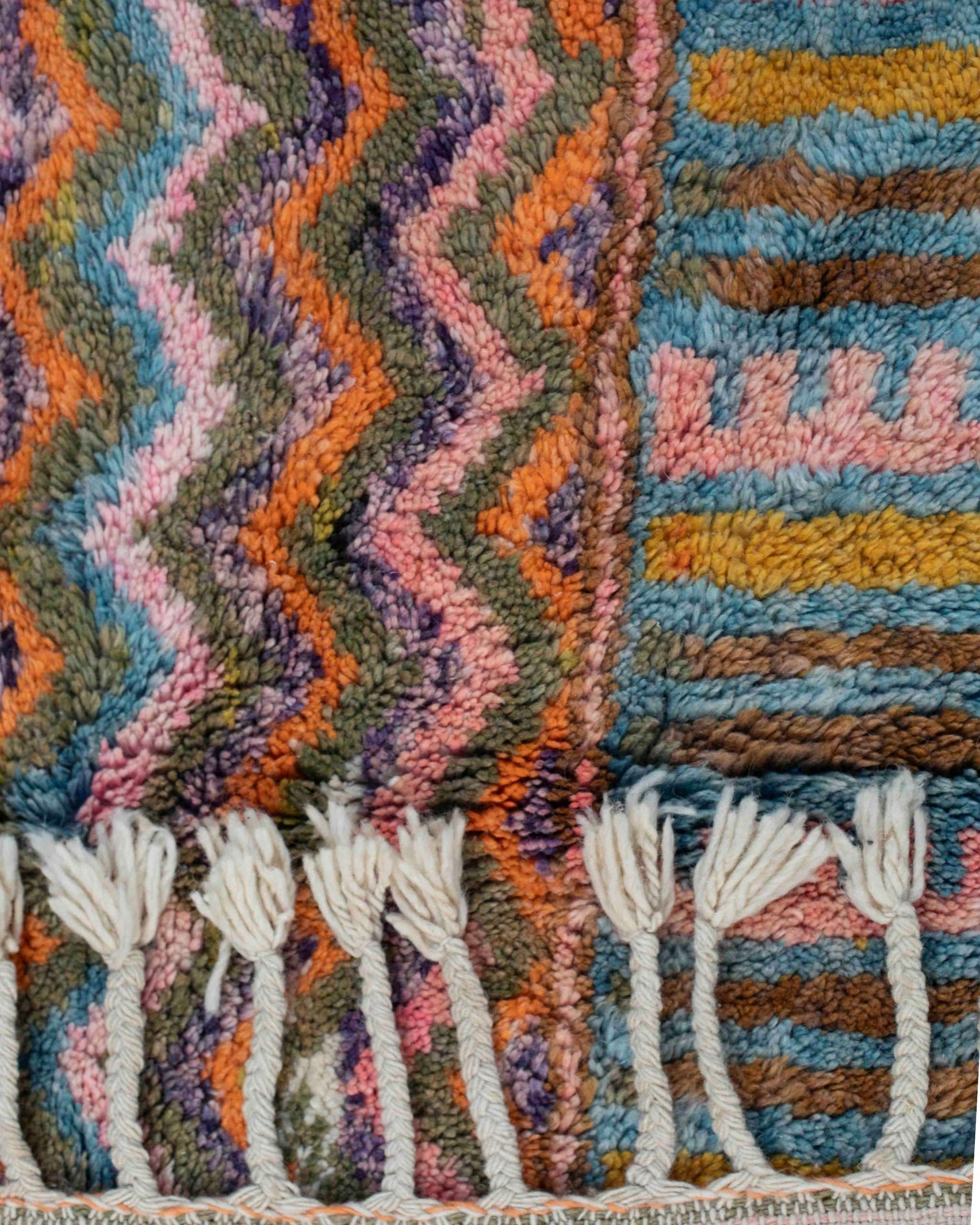 Dettaglio del vello del tappeto in lana colorata con fantasia zigzag e bordo con frange intrecciate