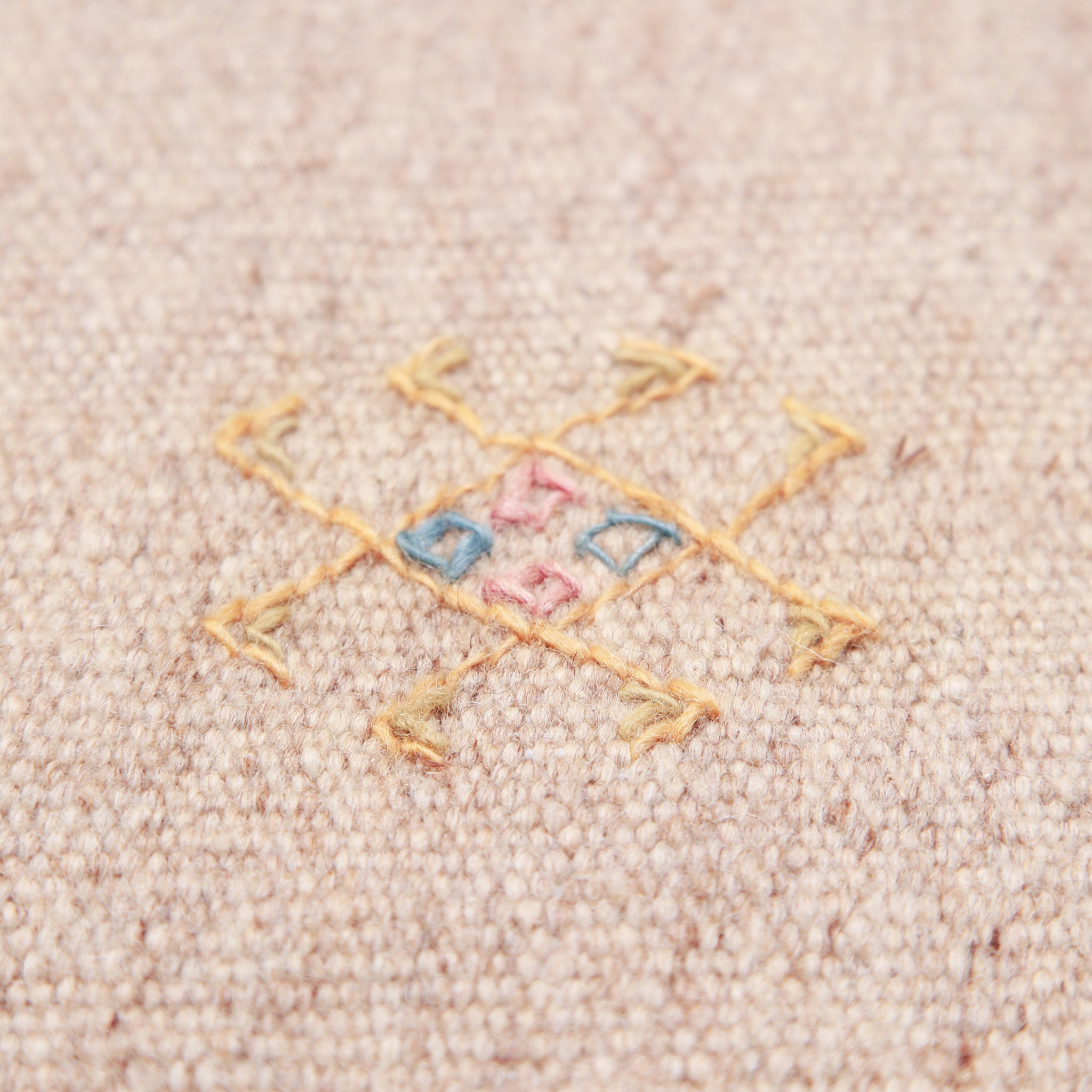 Primo piano motivo geometrico berbero su tappeto in lana, dettaglio ricamo artigianale in giallo, blu e rosa su base beige chiaro