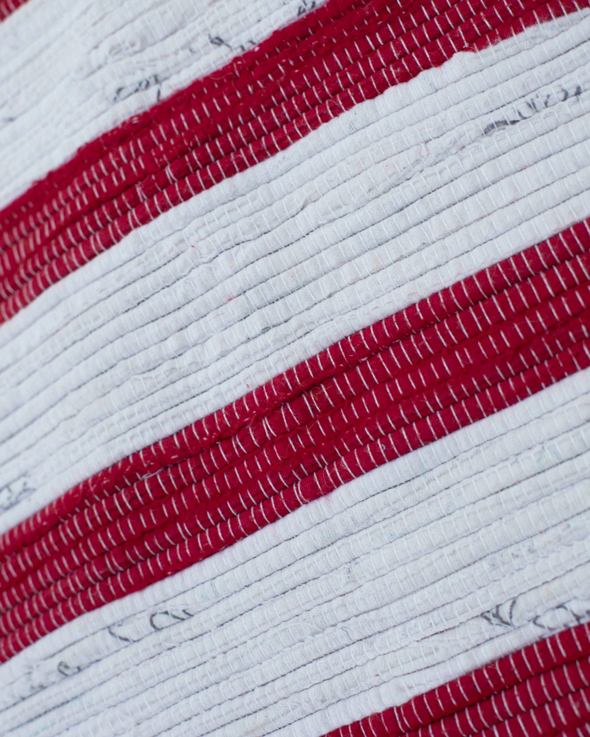 Dettaglio tappeto di stracci Boucherouite a righe rosse e bianche: tessuti misti riciclati annodati a mano, trama e micro-variazioni materiche