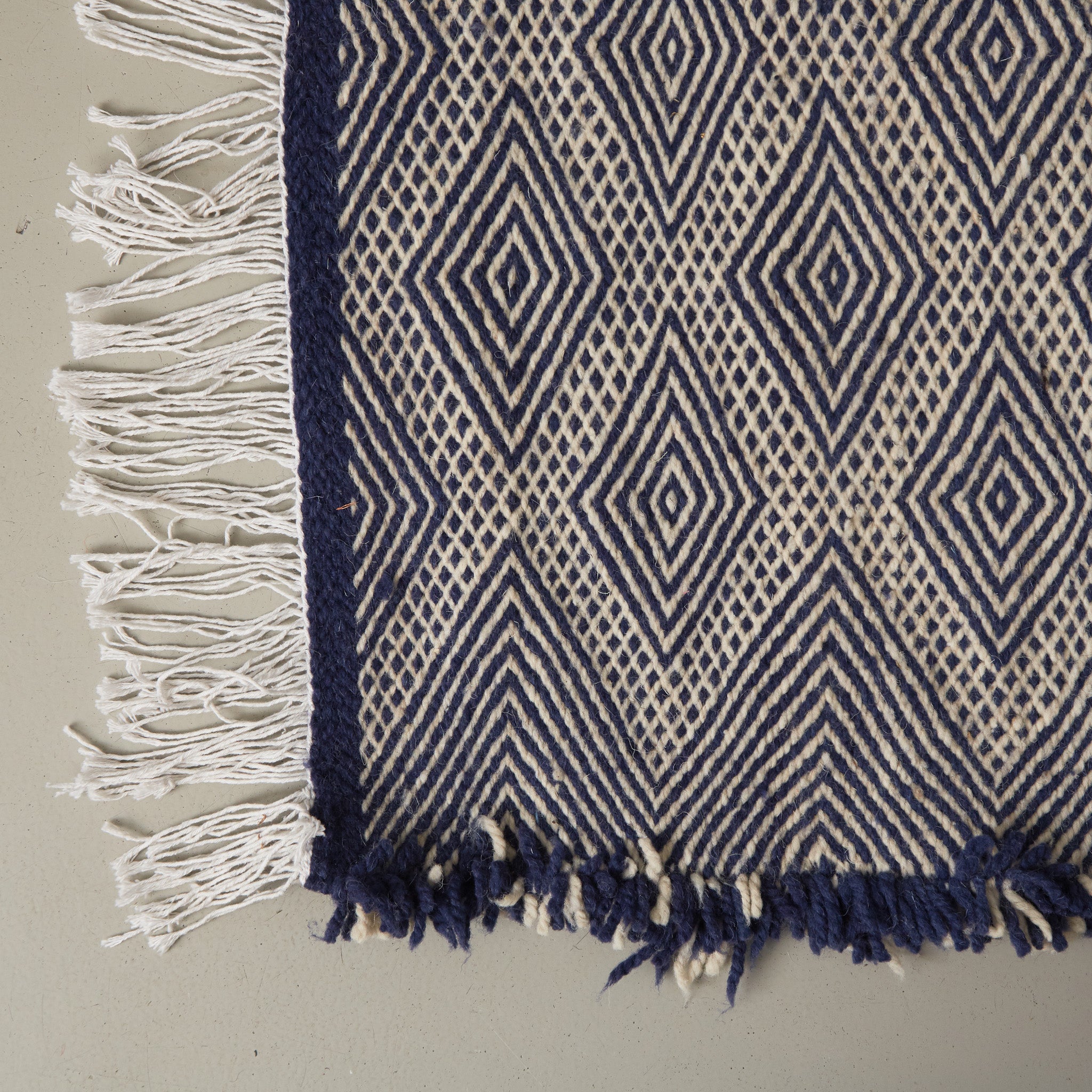 dettaglio dell'angolo e delle fragie di un tappeto zanafi kilim realizzato intrecciando lana color bianco e indigo creando dei rombi