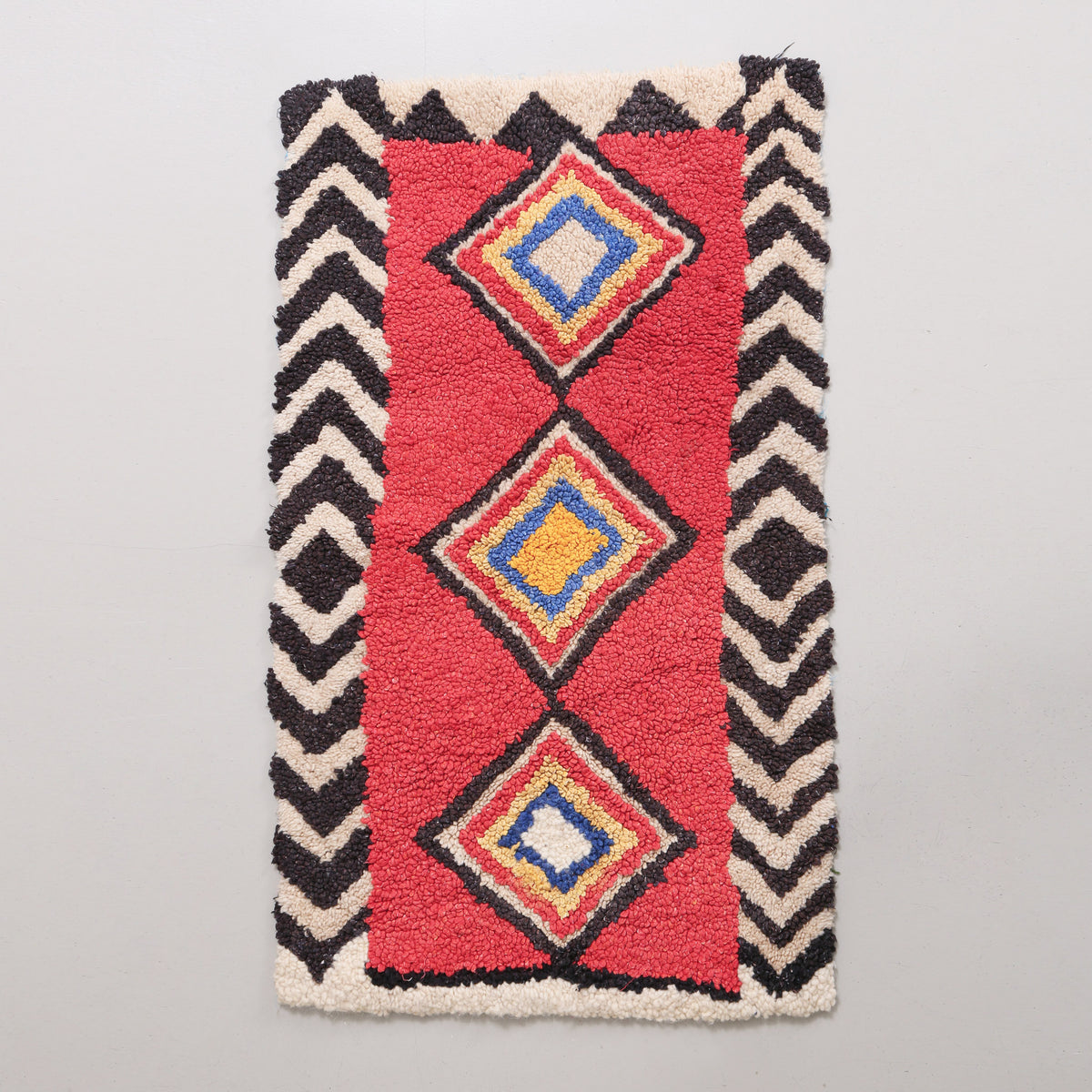 tappeto zindeck realizzato intracciando lana su un sacco di plastica. base in lana rossa con alla centro tre rombi colorati e bordi bianchi e neri