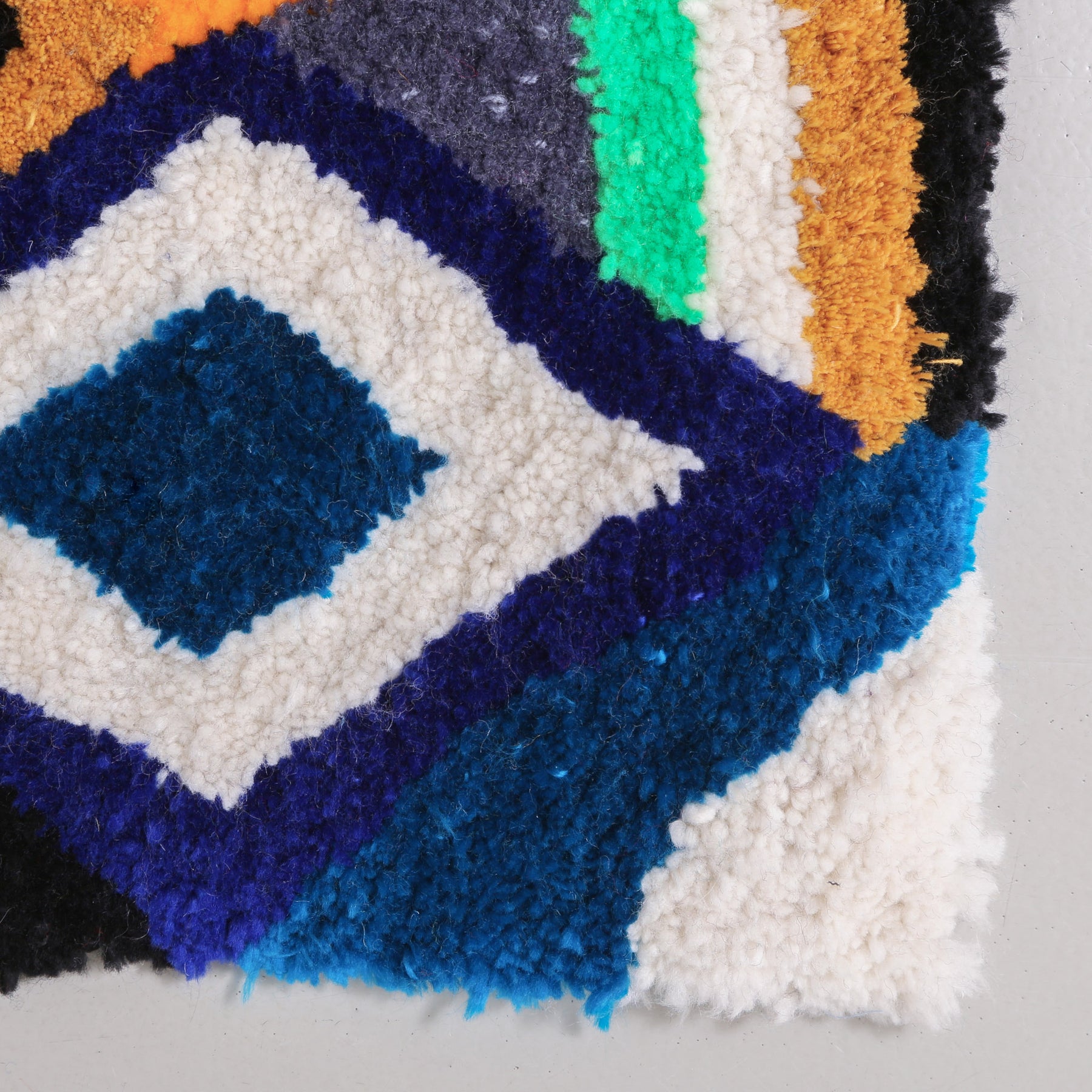 angolo di un tappeto zindekh con estremità bianca e azzurra, si vede un rombo blu e bianco e delle linee gialle bianche verde acqua e nero