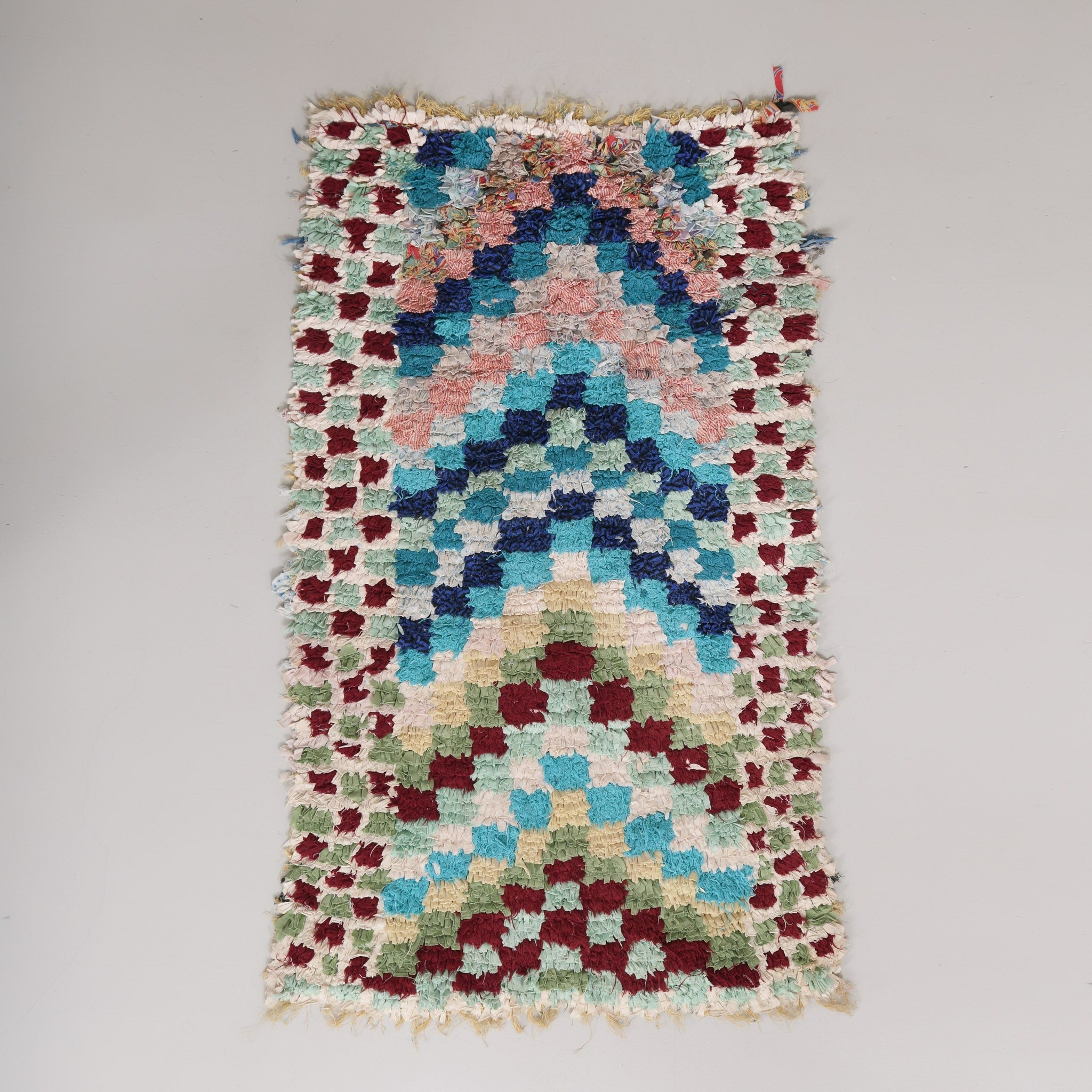 tappeto zyndekh con stracci di tessuto annodati su sacco di plastica che formano delle frecce a scacchi di diversi colori