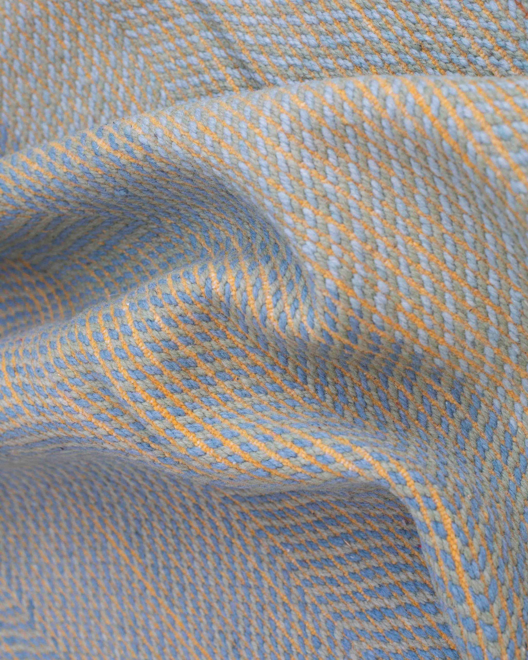 Texture e morbide pieghe del tappeto Zanafi in lana a tessitura piatta, effetto mélange azzurro e dorato