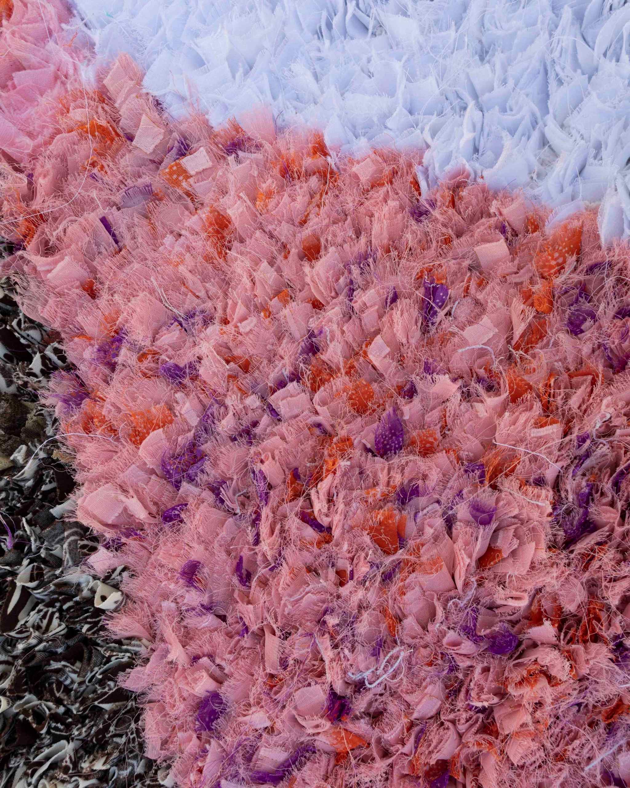 Texture ravvicinata della parte rosa del tappeto Boucherouite con frammenti di tessuto leggeri e inserti arancioni e viola