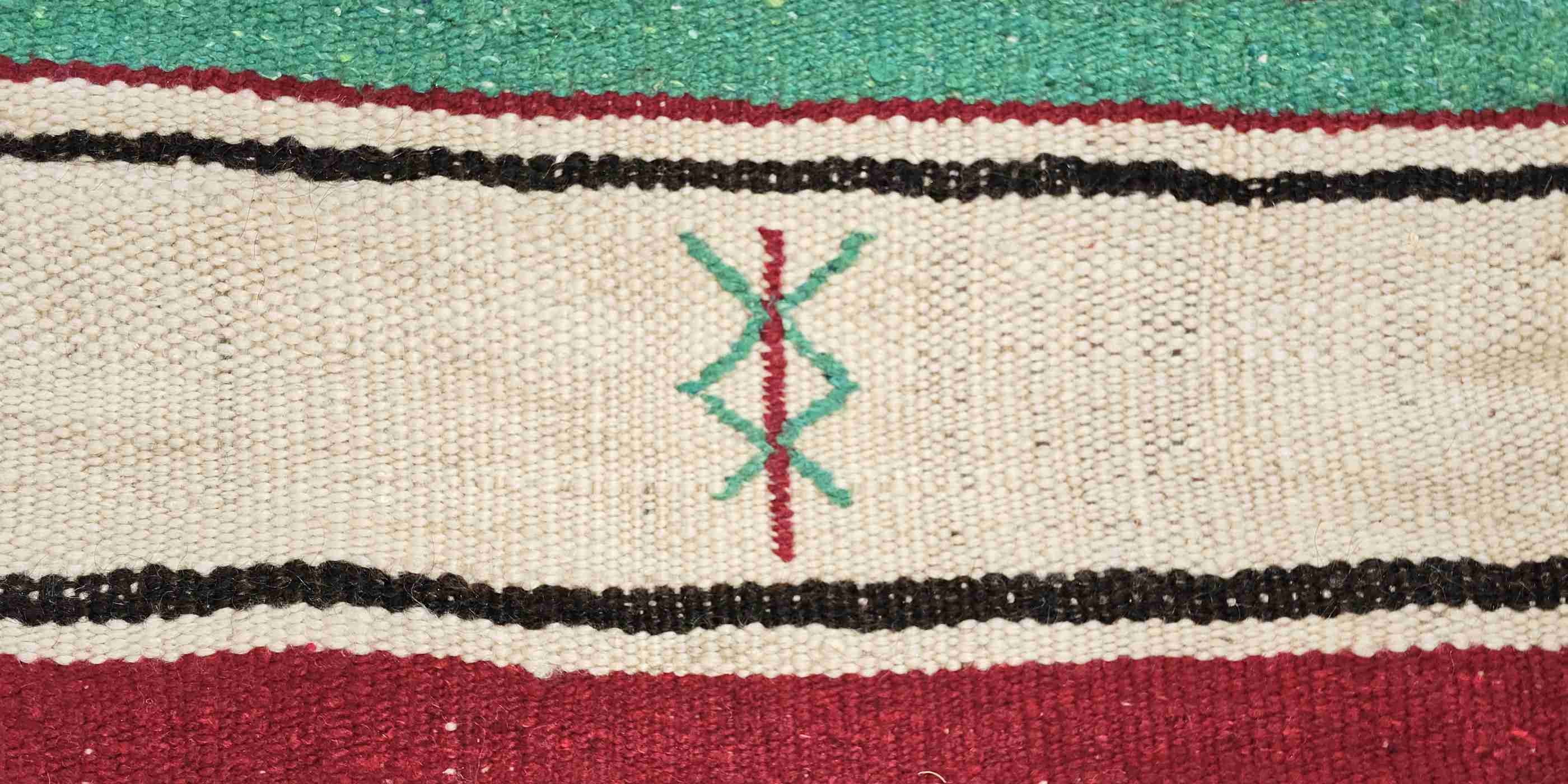 dettaglio di una coperta marocchina vintage in lana con line superiore verde e linea interiore bordeaux con un simbolo centrale