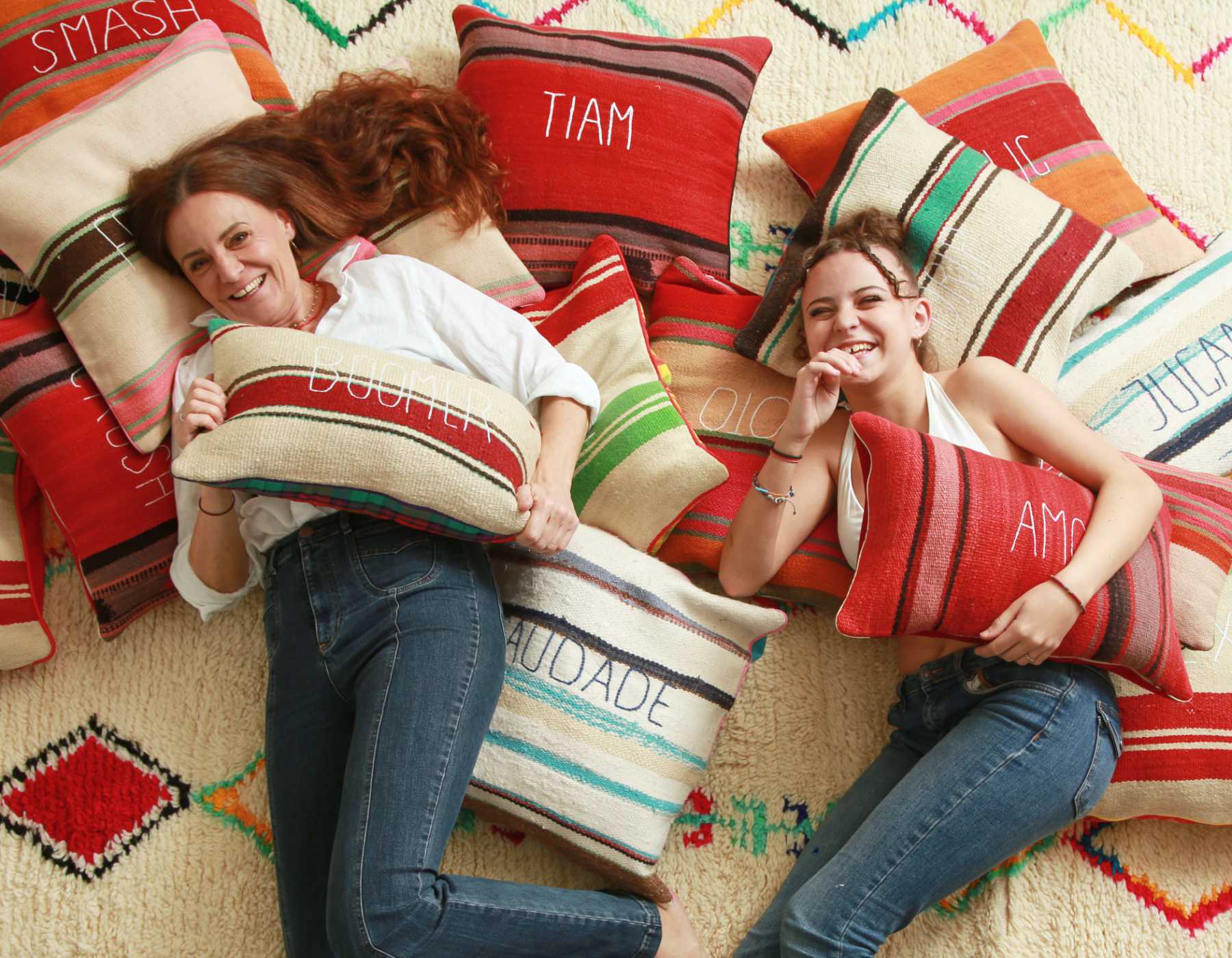 sabina maffei plozner e sua figlia costanza sorridono mentre tengono in mano dei cuscini della collezione tra le righe stando sdraiate su un tappeto ricoperto di cuscini