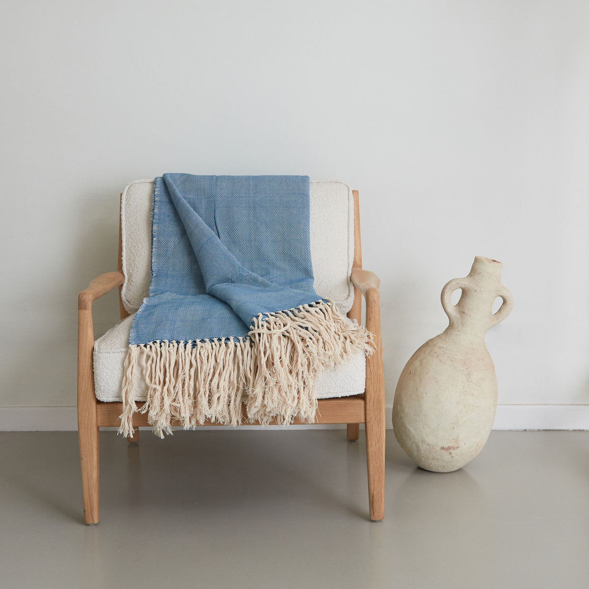 coperta d'arredo in cotone color blu jeans con frange appoggiata su una poltrona