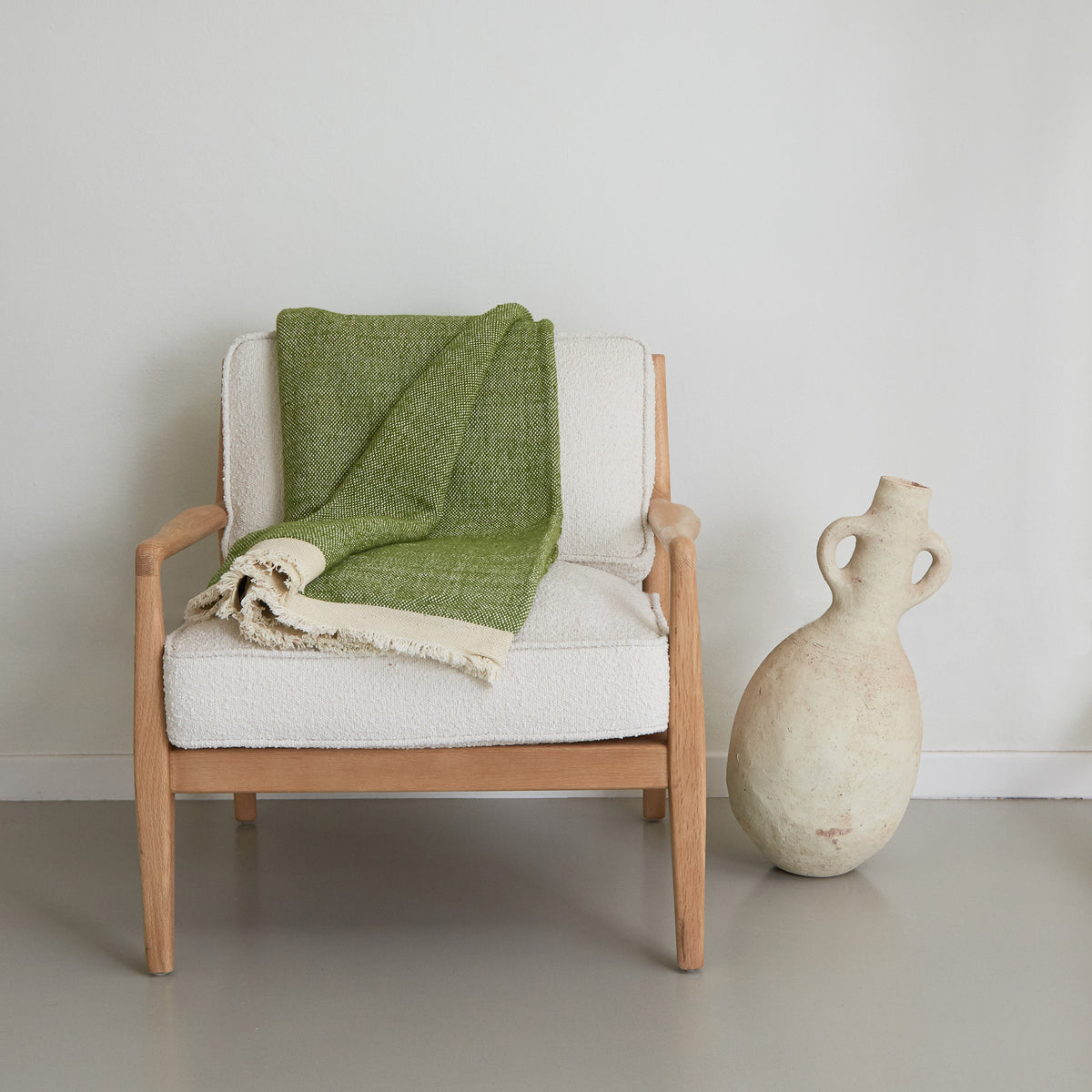 coperta d'arredo realizzata  mano in lana e cotone color verde pappagallo con corta frangia bianca distesa su una sedia