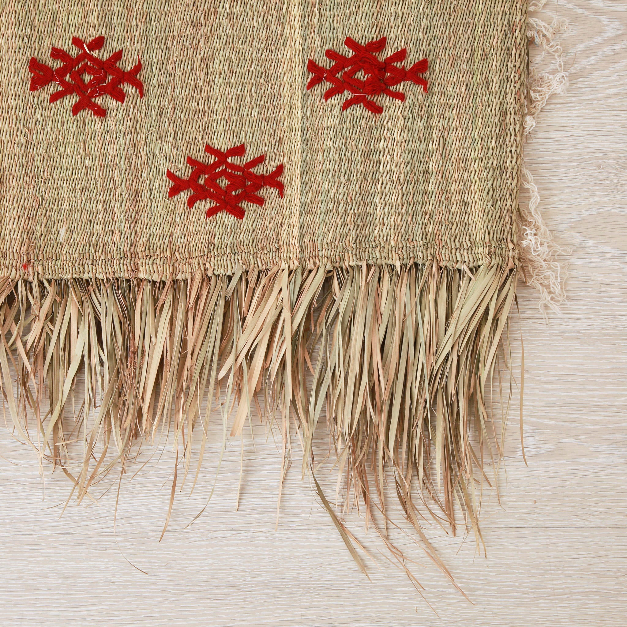 dettaglio dell'angolo di una piccola stuoia hassira intrecciata con paglia di palma e ricamata con simboli in lana rossa