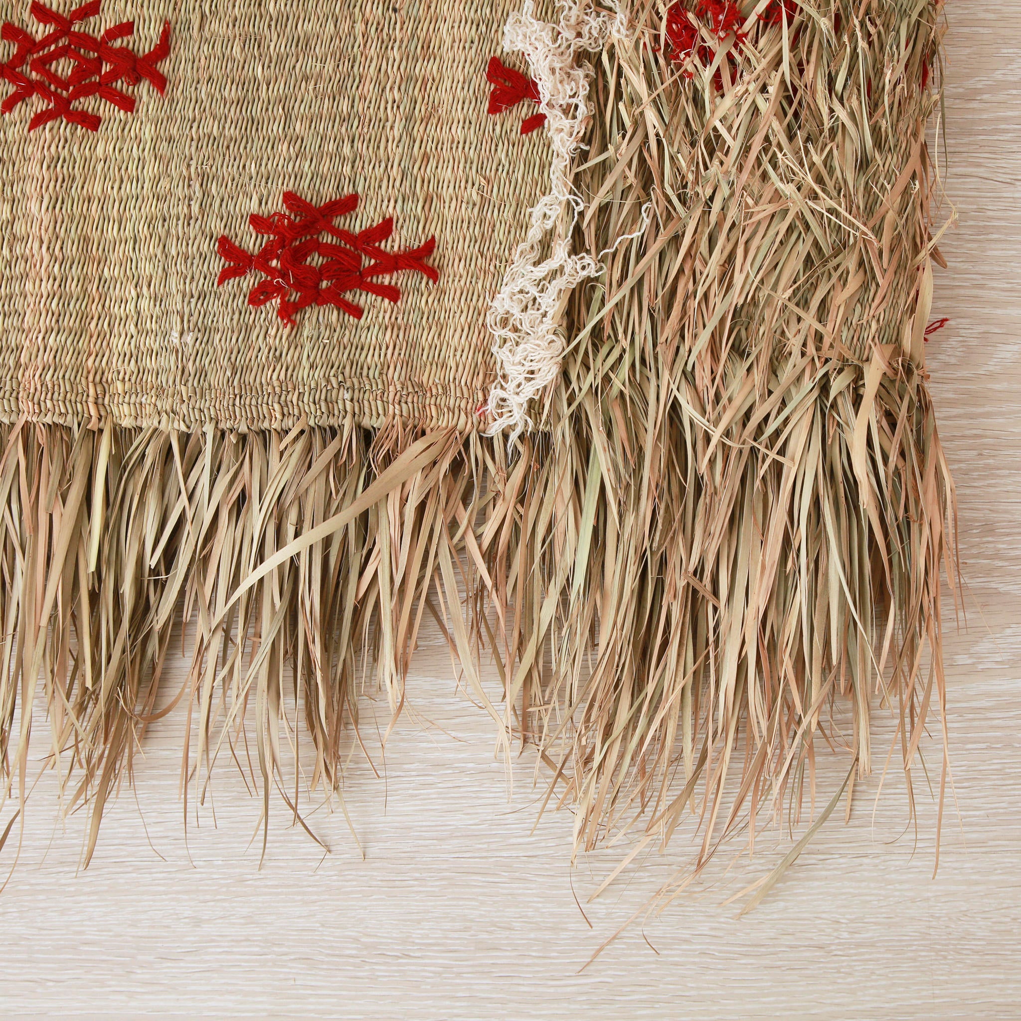 dettaglio del retro di una piccola stuoia hassira intrecciata con paglia di palma e ricamata con simboli in lana rossa