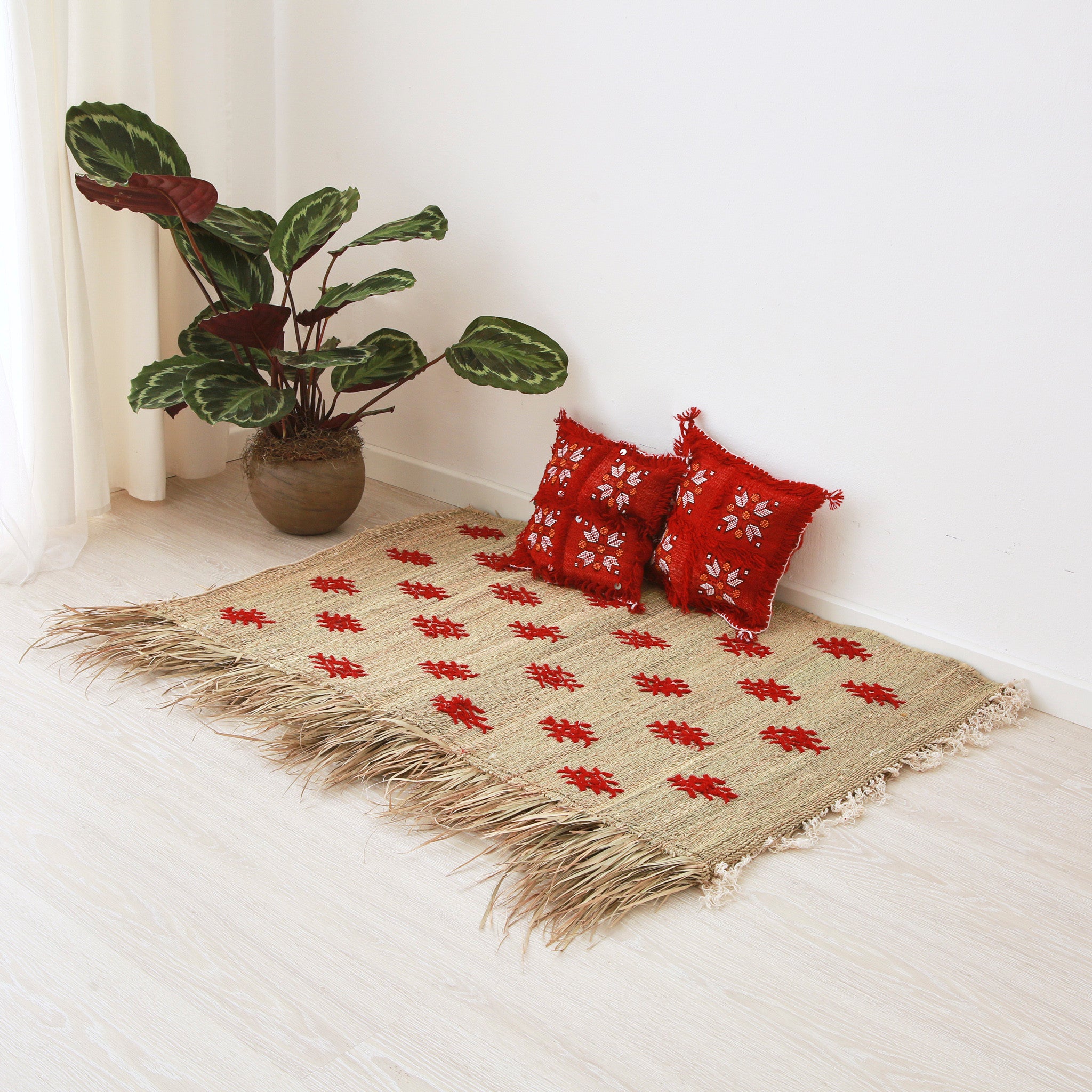 piccola stuoia hassira intrecciata con paglia di palma e ricamata con simboli in lana rossa su pavimento con due piccoli cuscini rossi e quadrati sopra