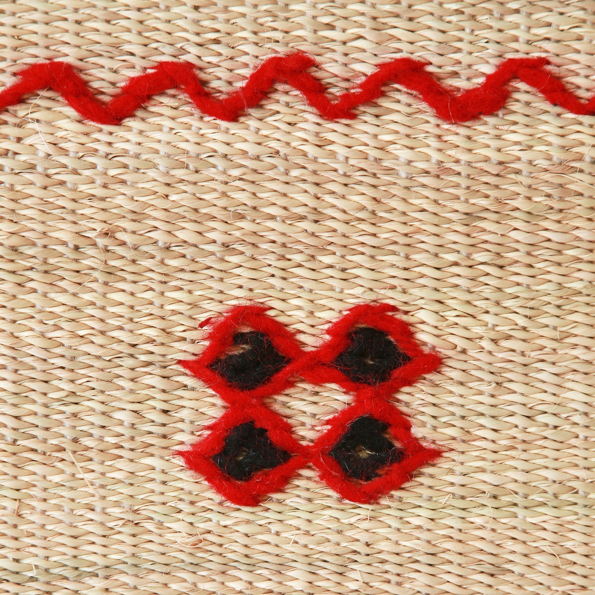 dettaglio del ricamo di una stuoia hassira intrecciata a mano con paglia di palma e ricamata con con lana rossa e nera.