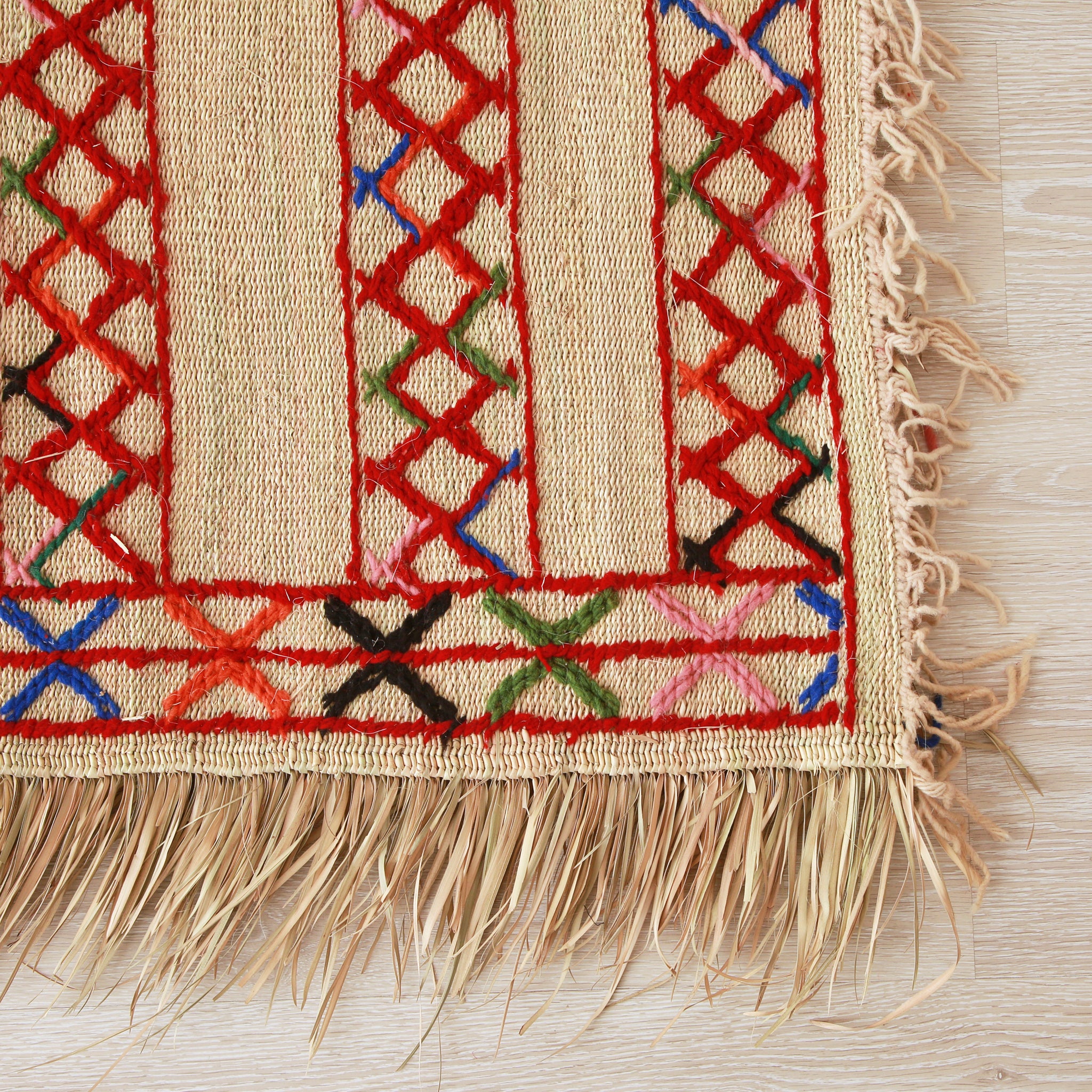 angolo di una stuoia hassira in paglia di palma con ricami in lana rossa blu verde e rosa