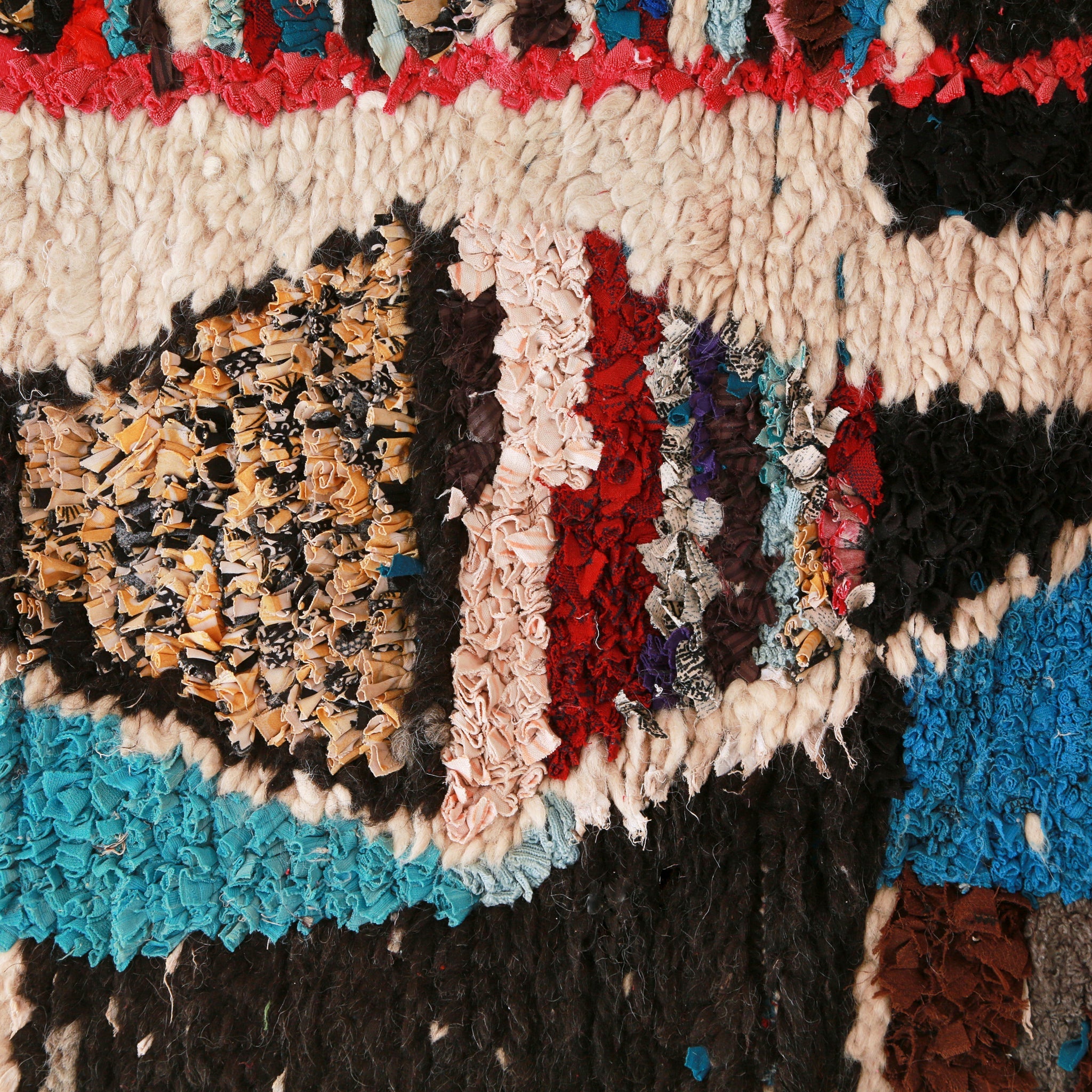 dettaglio di una figura geometrica che ricorda un triangolo formata da stracci di tessuto colorati, intorno della lana bianca e nera