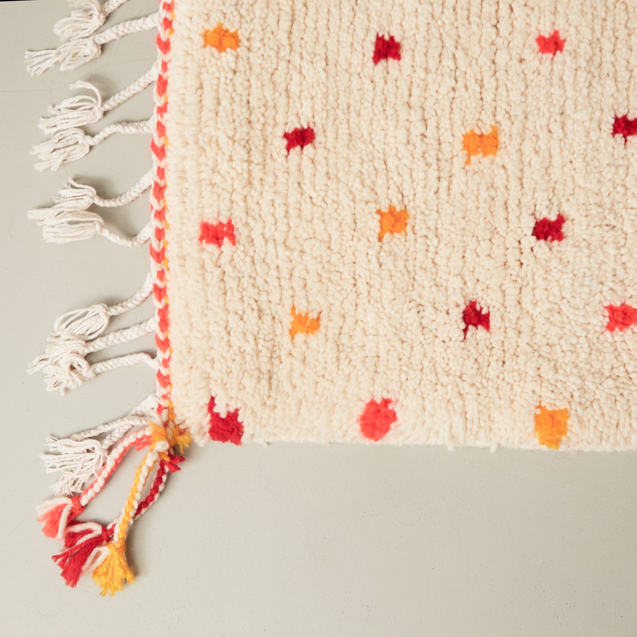 dettaglio dell'angolo e della frangia colorata di un tappeto azilal in lana chiara con pois gialli rossi arancioni