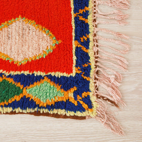 angolo di un tappeto azilal vintage che mostra la cornice in lana blu con bordi in giallo chiaro e rombi colorati all'interno
