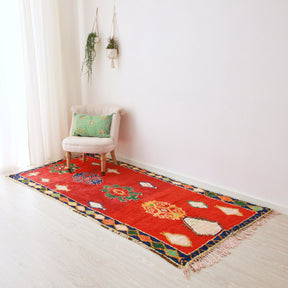 tappeto azilal vintage tessuto con lana rossa appoggiato sul pavimento. Sul tappeto c'è una poltrona in tessuto chiaro con un cuscino si sabra color verde acquamarina