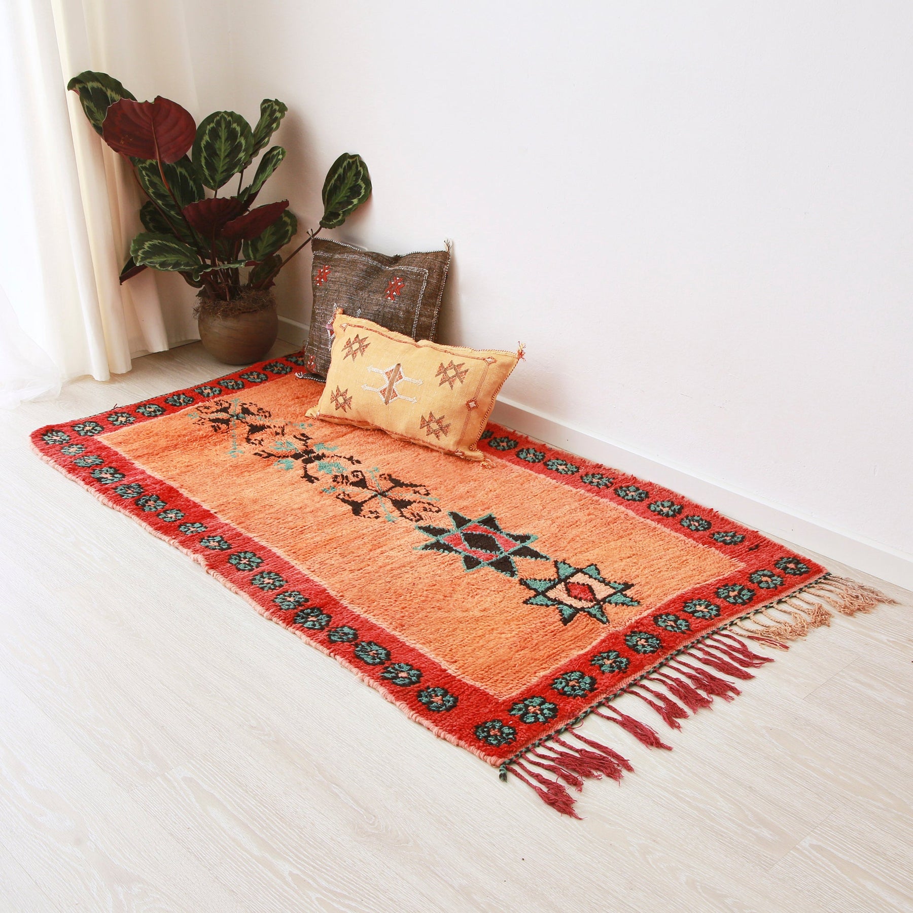 tappeto azilal vintage per corridoio con lana arancione, con cornice rossa e disegni centrali disteso sul pavimento. Sul tappeto c'è un tappeto giallo, uno marrone scuro e una pianta
