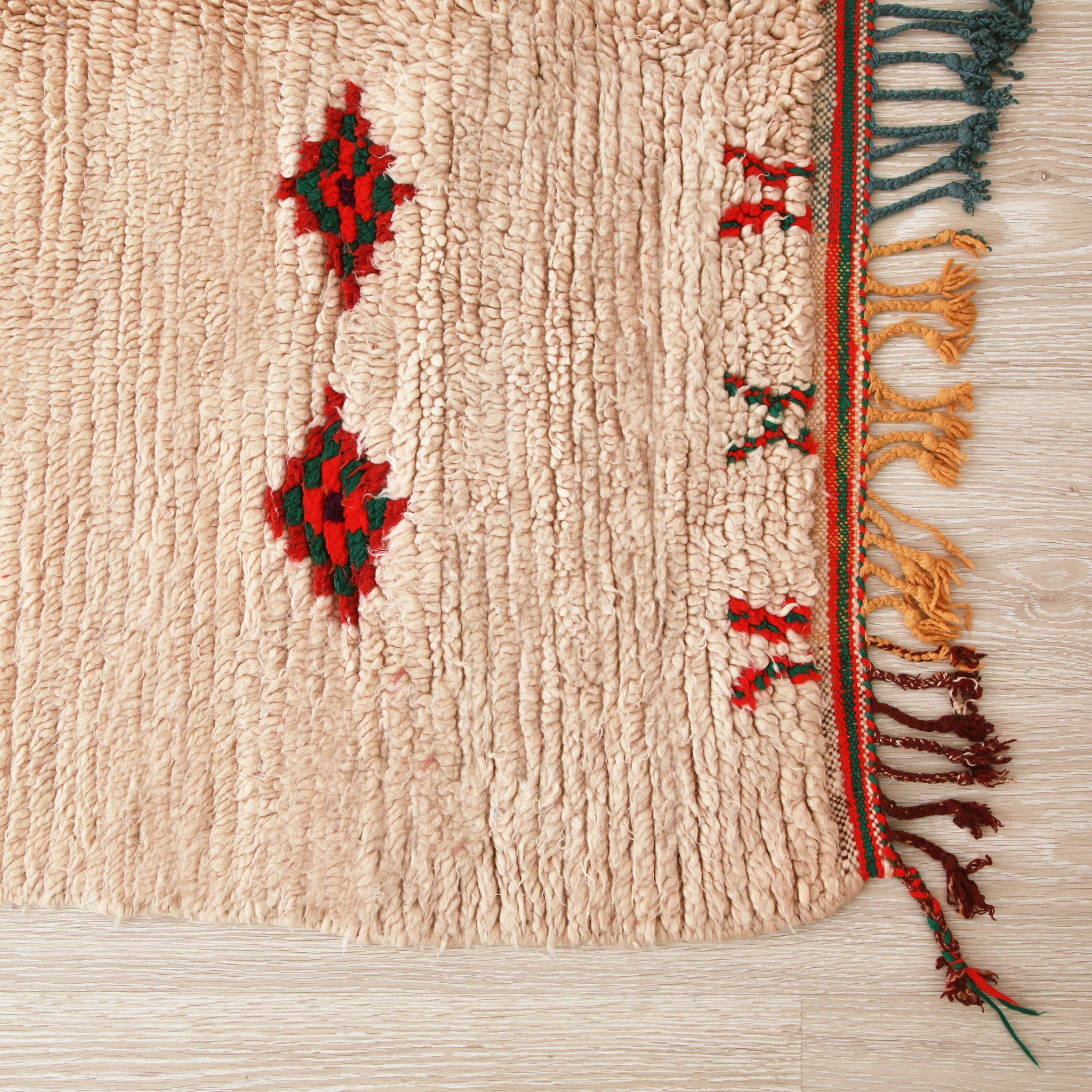 angolo di un tappeto azilal vissuto su lana bianca con piccoli disegni,la frangie è rosso scuro e gialla